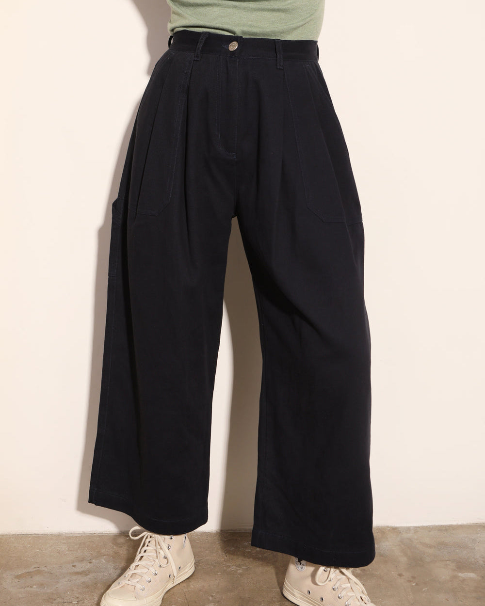 Person wearing black wide-leg pants and a green top against a white wall.