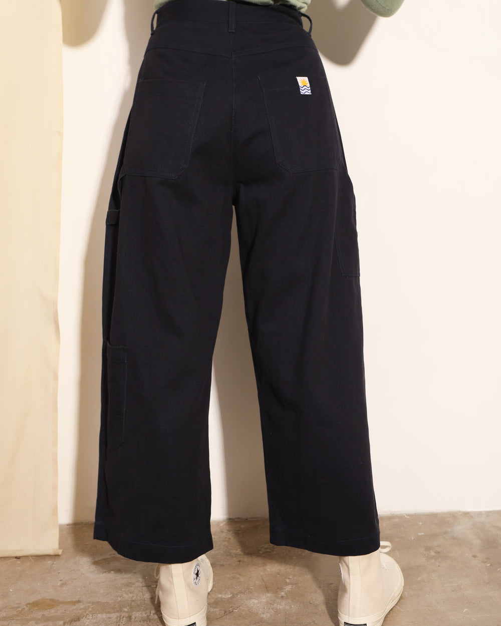 Person wearing black pants with a visible brand logo against a plain background