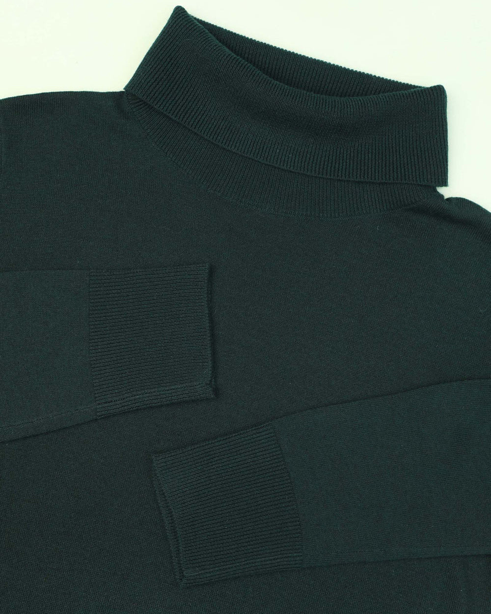Close-up of a dark green turtleneck sweater with patch details on a light background