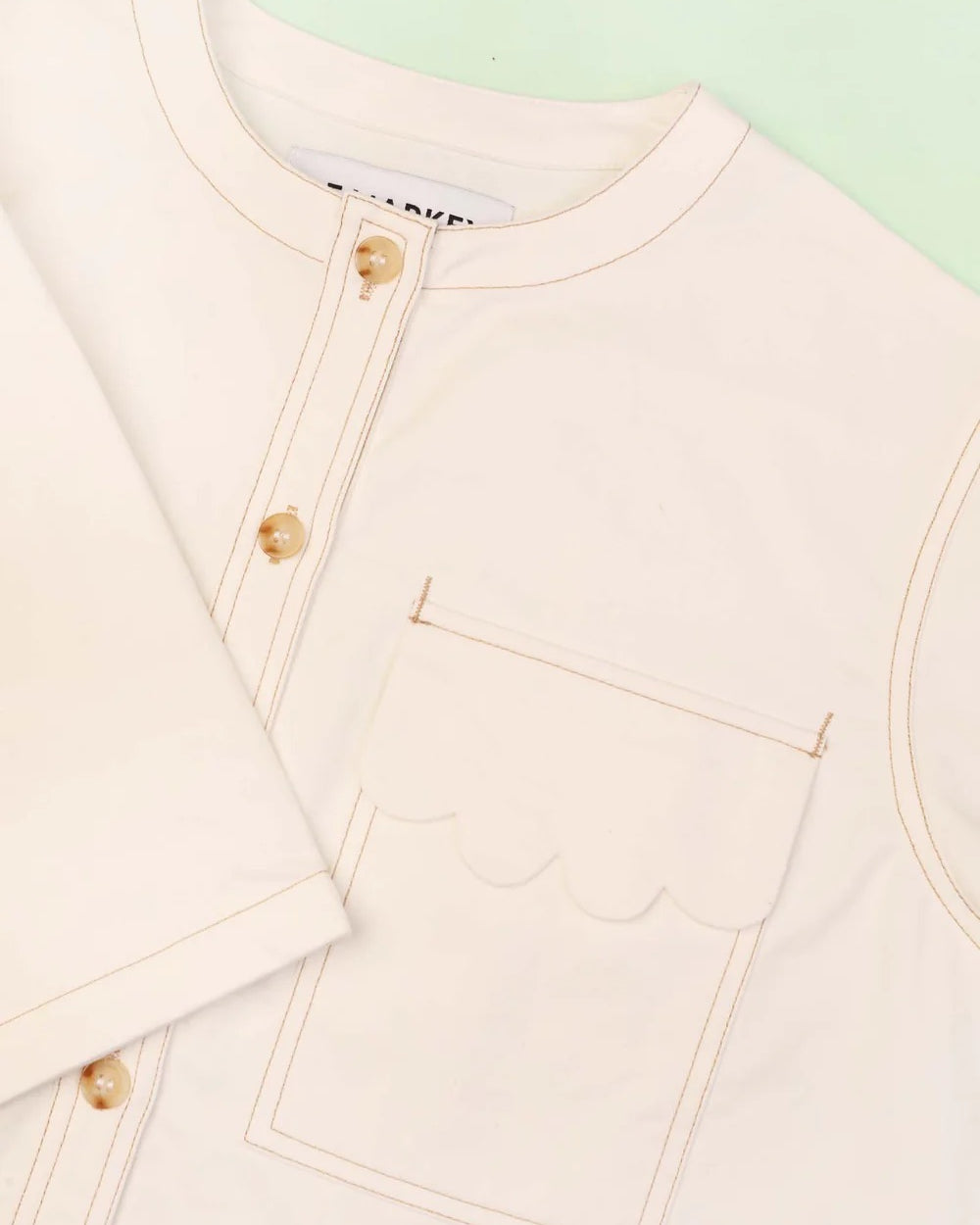 Close-up of a light pink jacket with gold buttons on a light green background