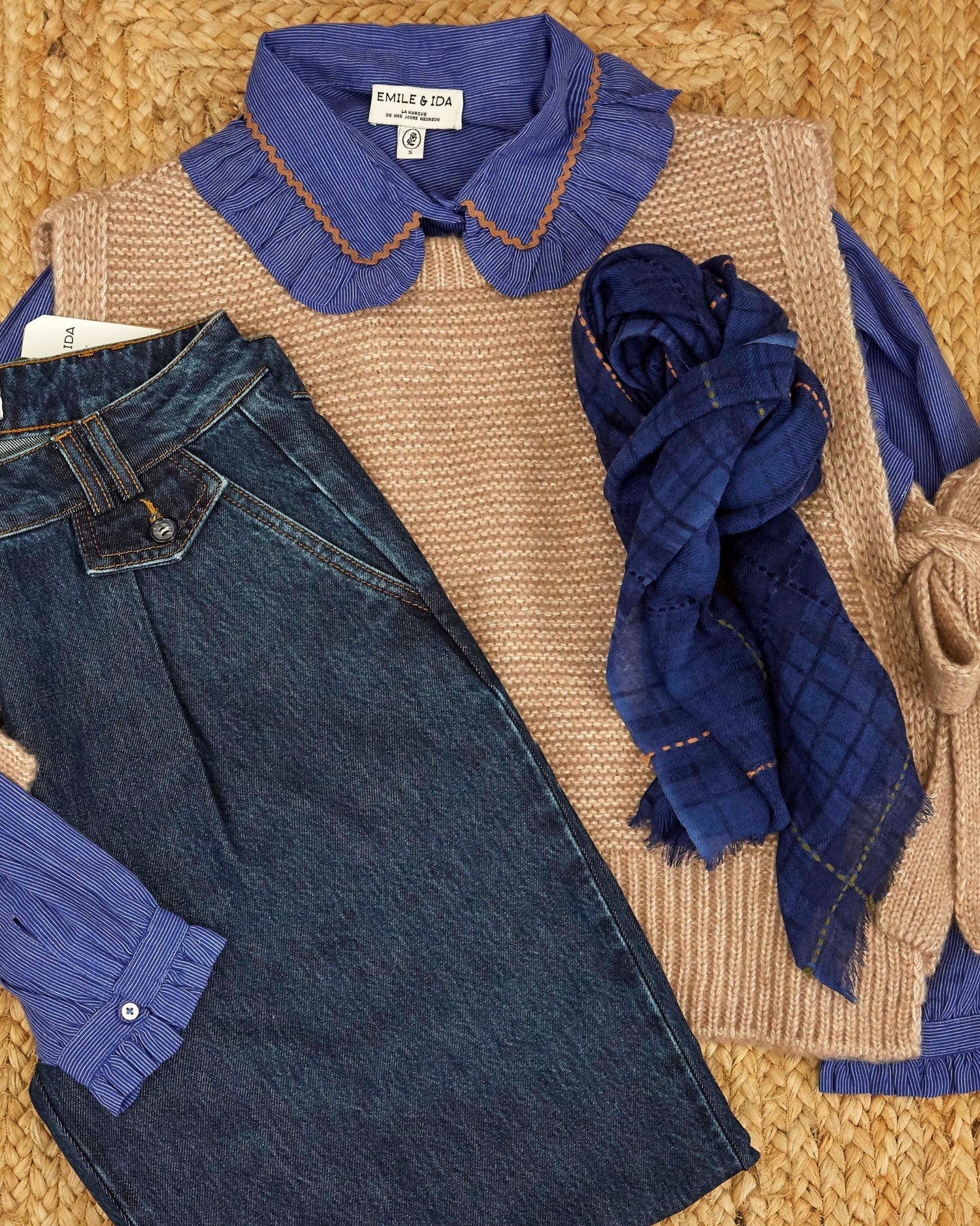 Knitted sweater with blue collar, jeans, and blue scarf on a textured surface