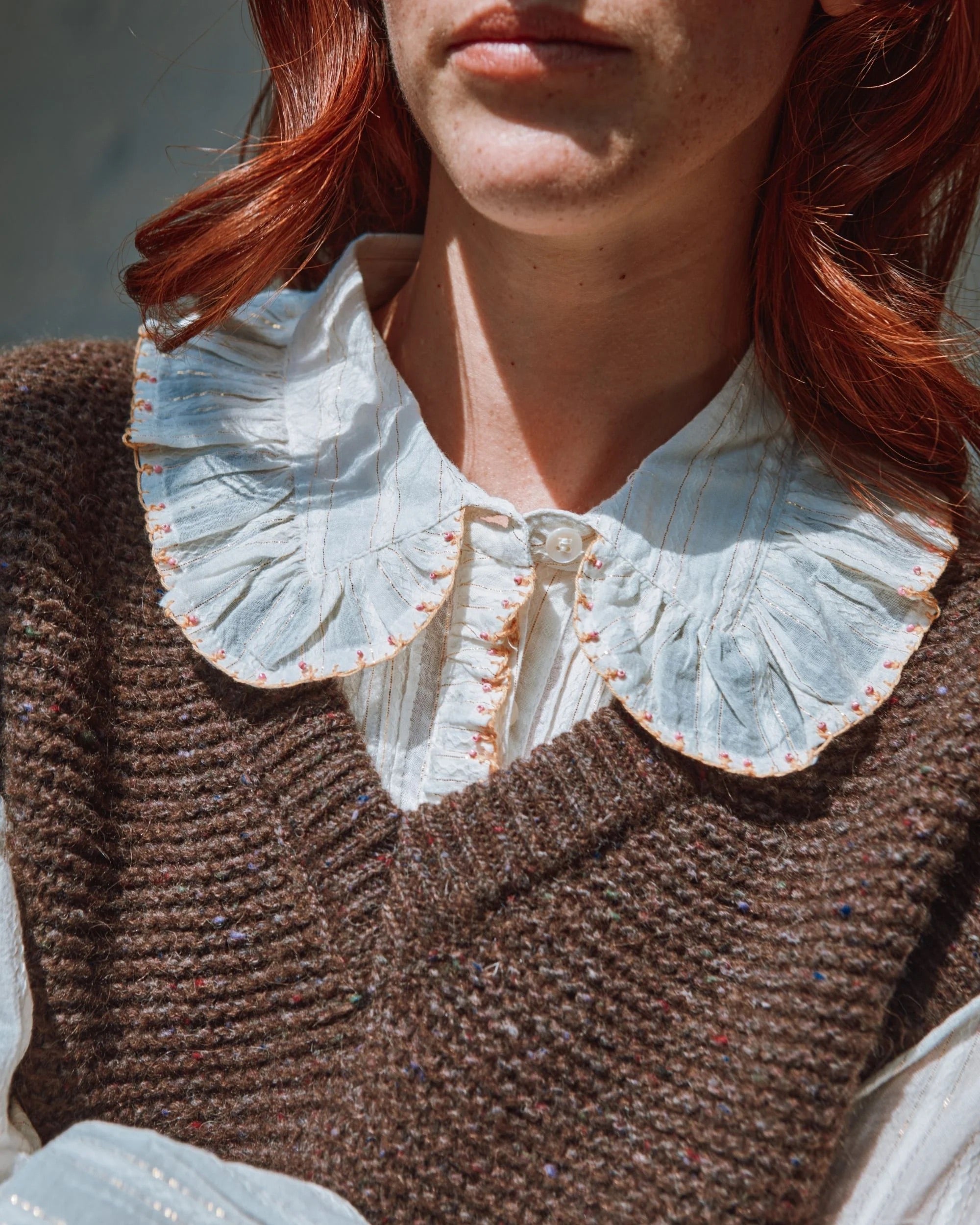 Close-up of a person wearing a brown sweater with a white lace collar.