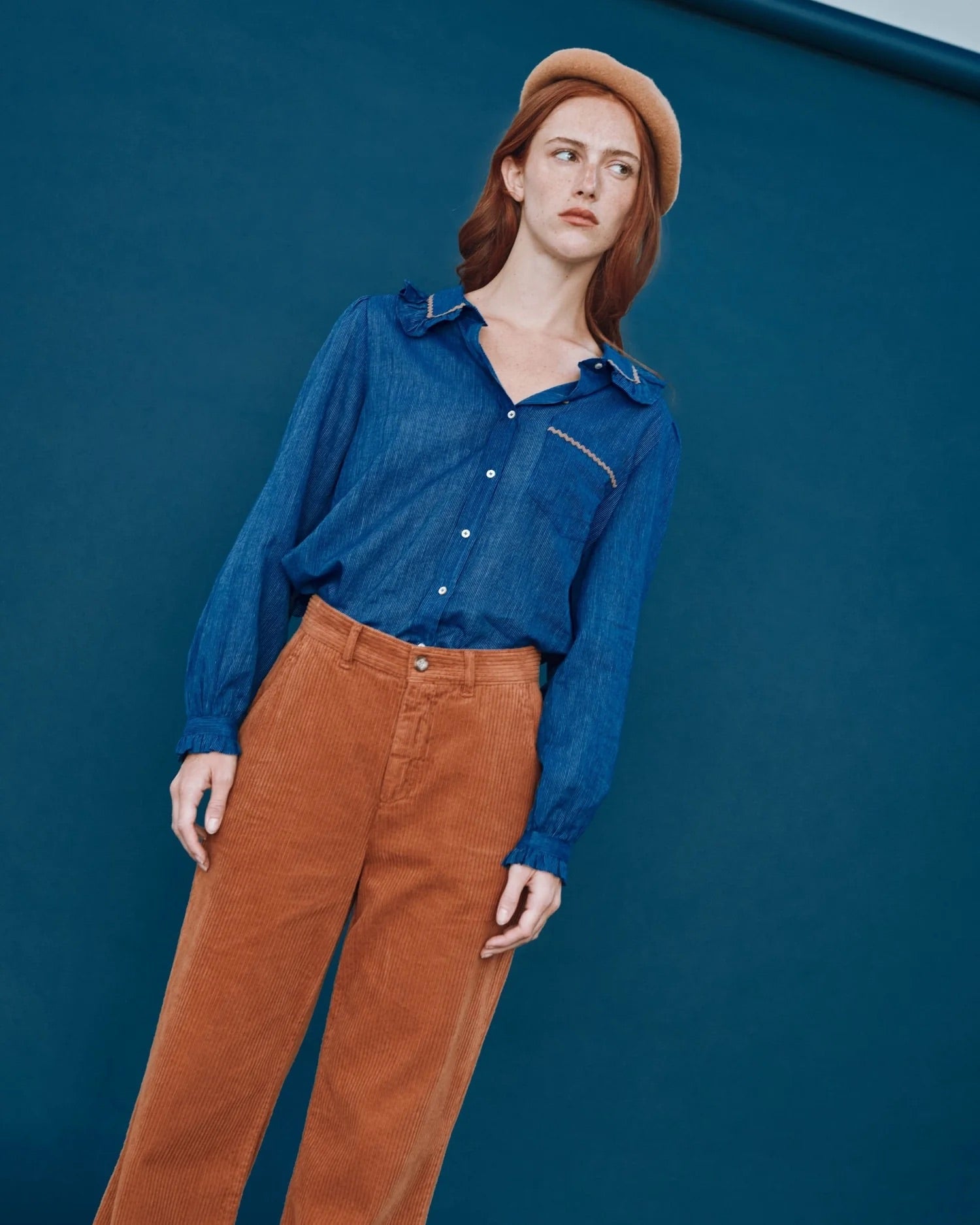 Woman wearing a blue shirt and brown pants against a blue background