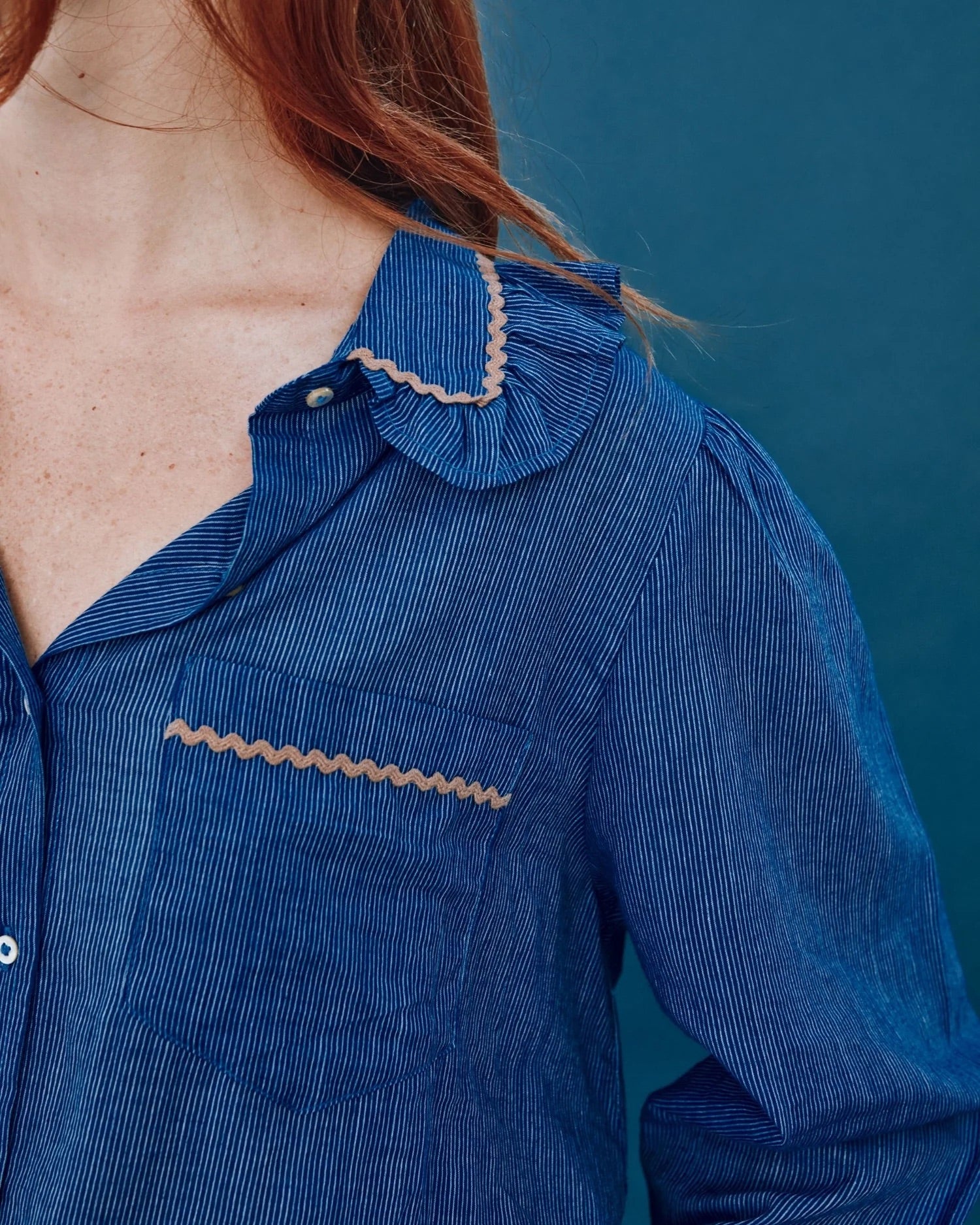Close-up of a person wearing a blue dress with decorative trim against a blue background