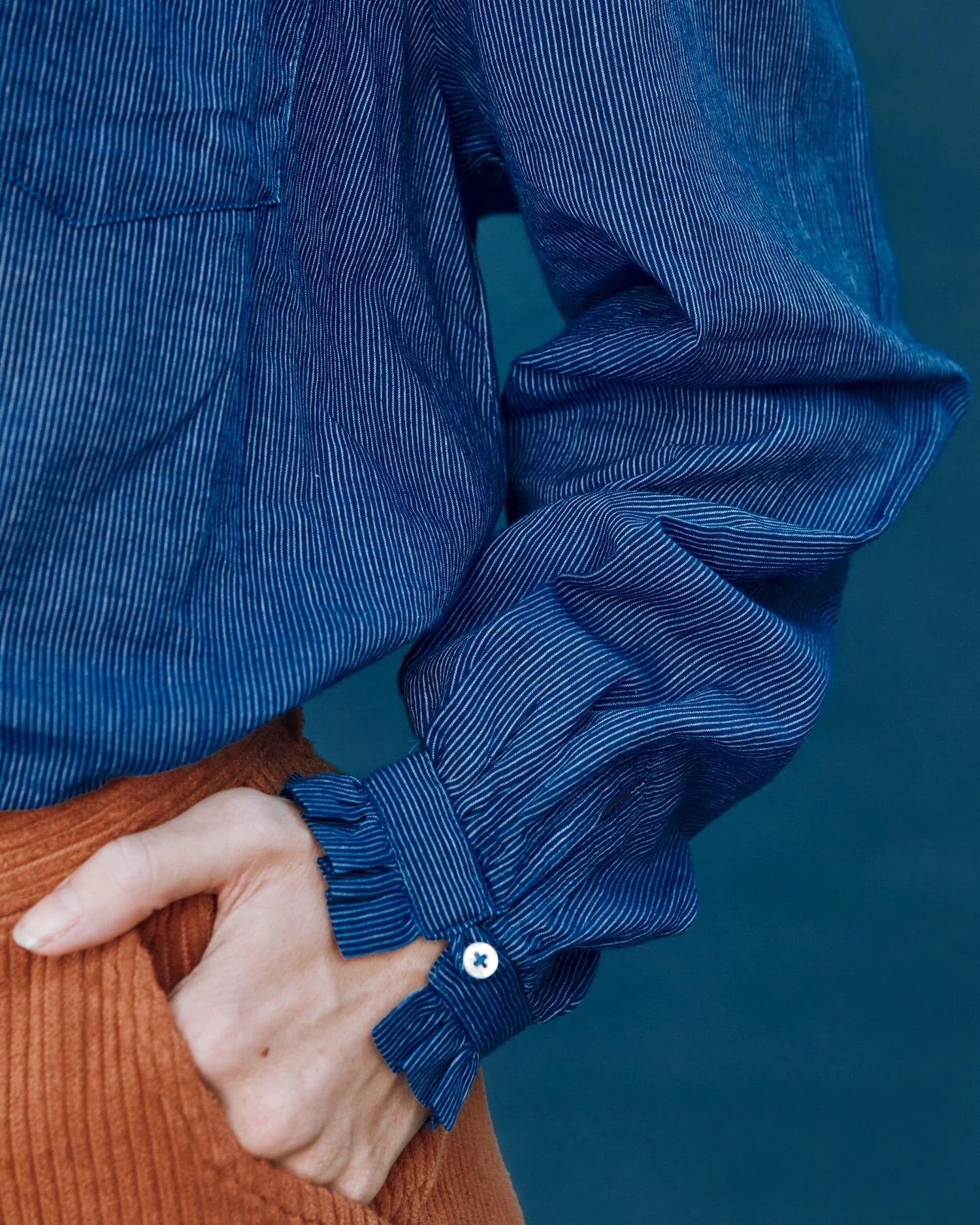 Close-up of a person wearing a blue striped shirt with rolled-up sleeves against a dark background