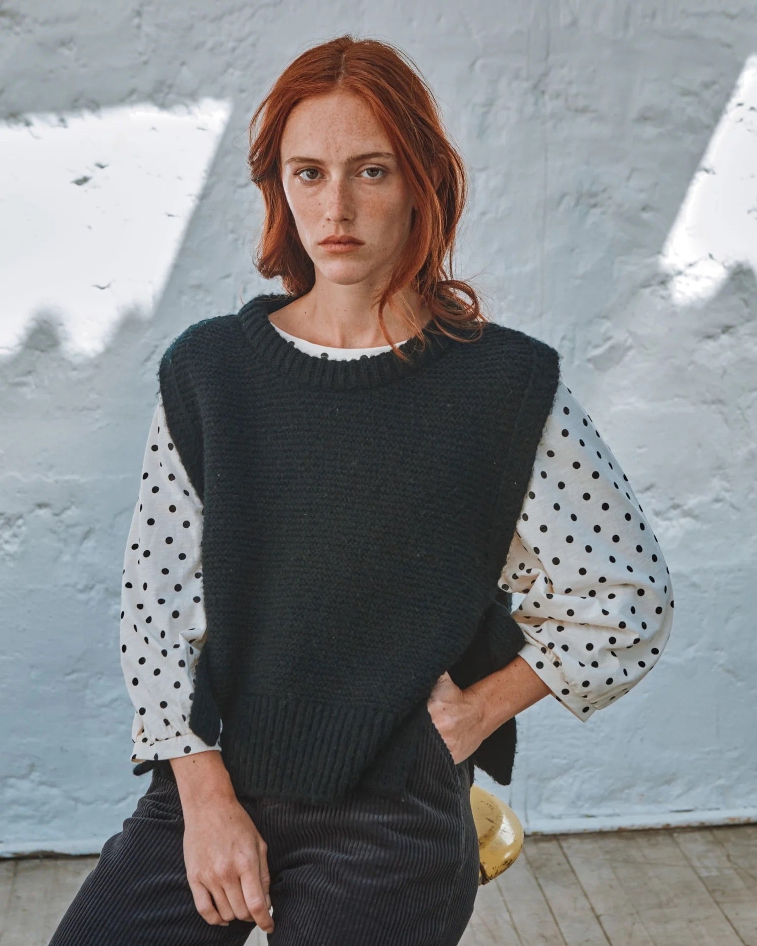 Woman wearing a black sweater with polka dot sleeves against a textured wall.