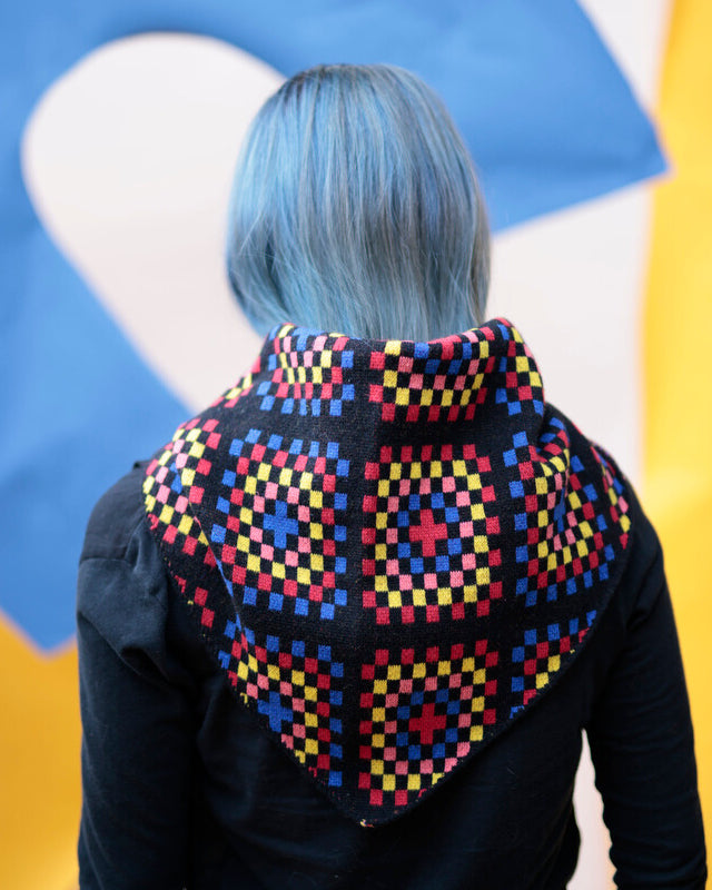 Person wearing a colorful geometric patterned shawl with a multicolored background