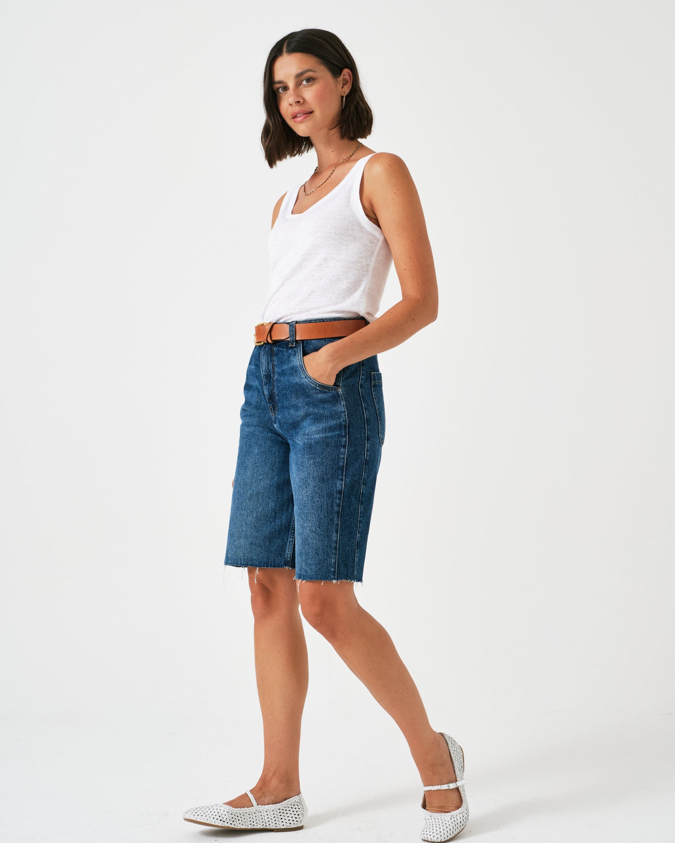 Woman wearing a white tank top and blue denim shorts on a white background