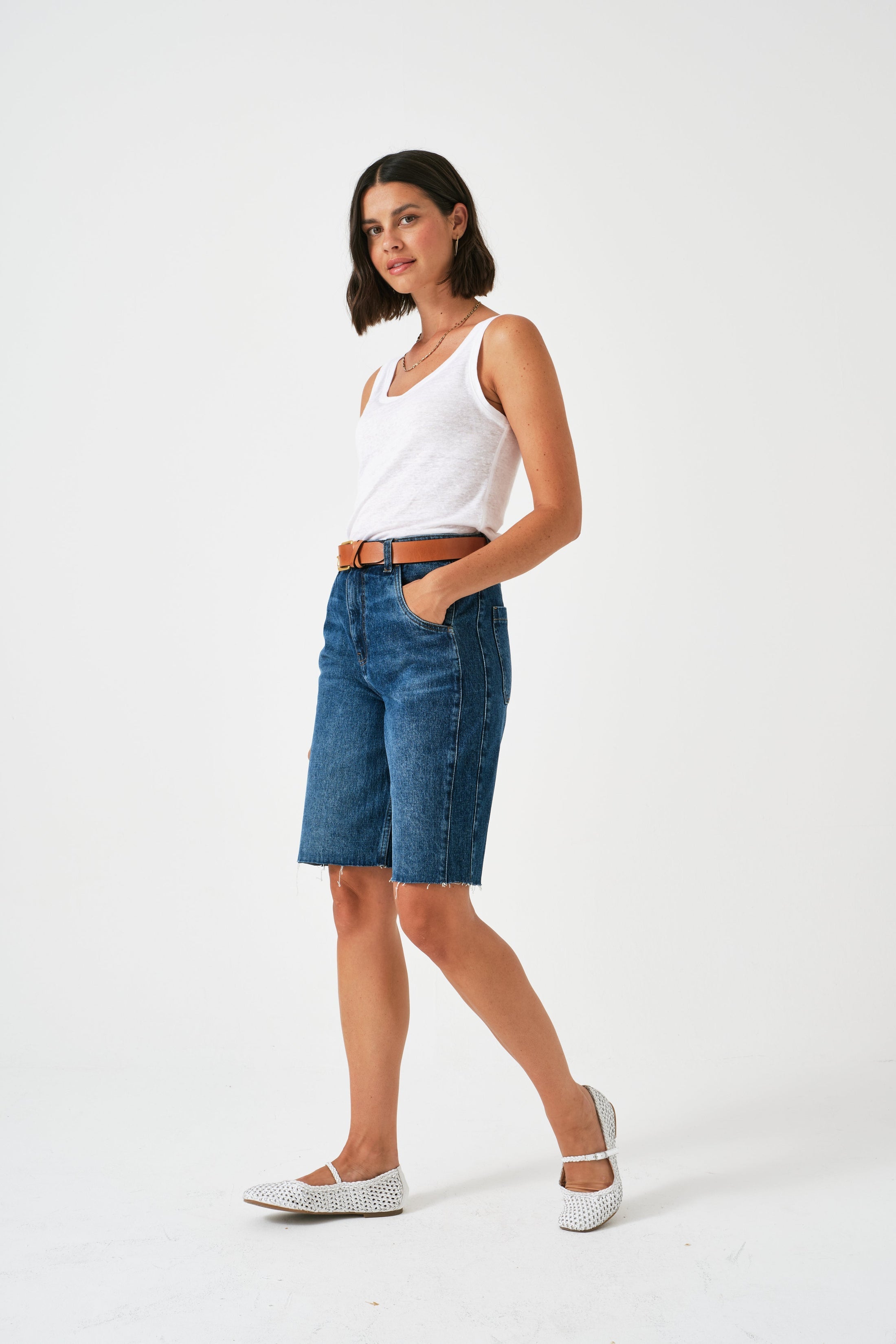 Woman wearing a white tank top and blue denim shorts on a white background
