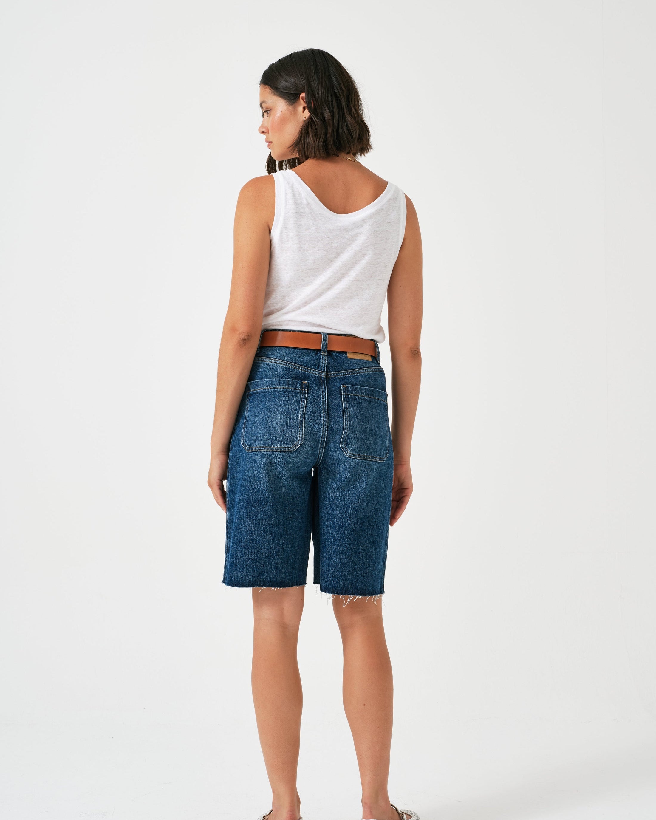 Woman wearing a white sleeveless top and blue denim shorts on a white background