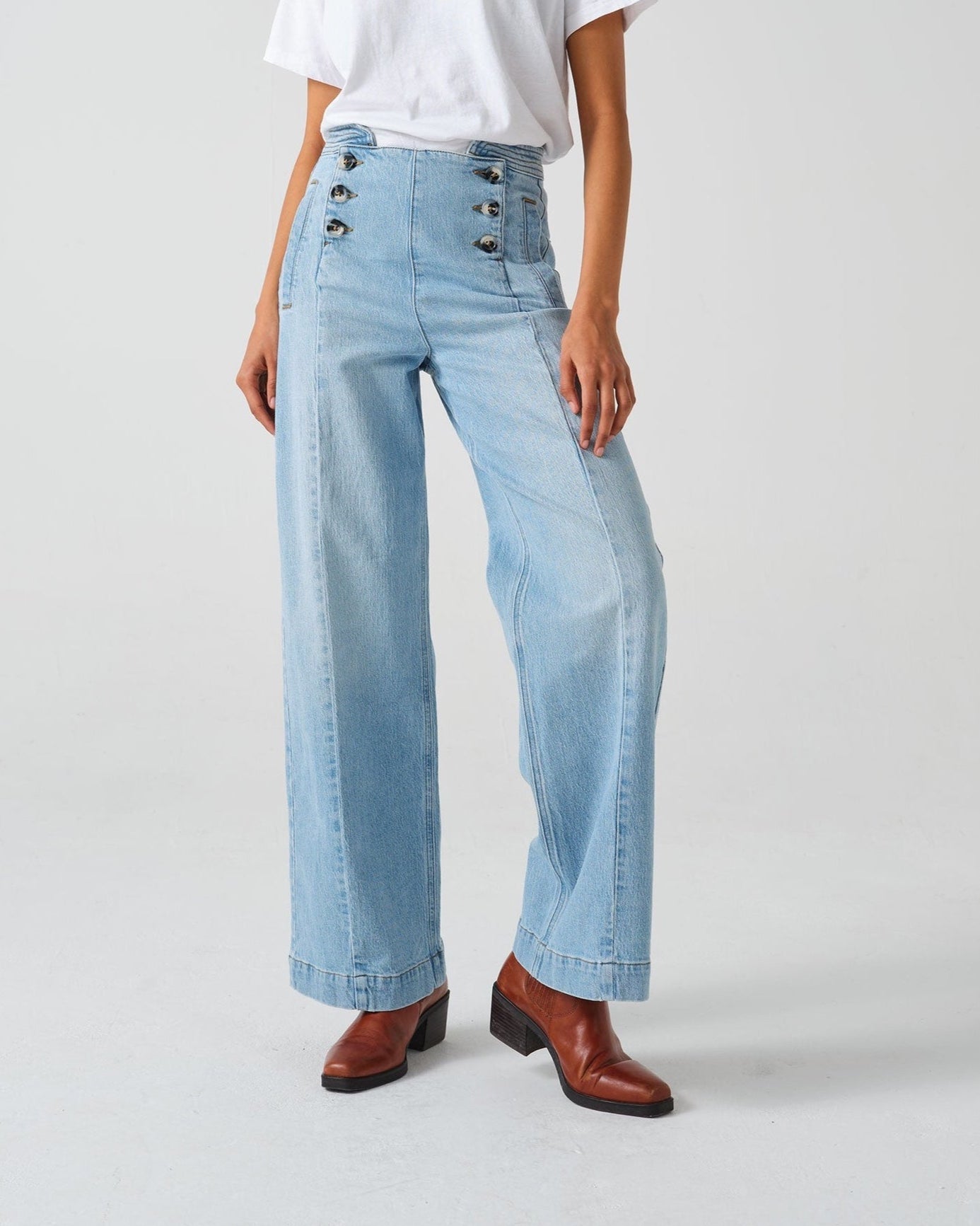 A pair of high-waisted, wide leg jeans with a button-up front in an oceanic blue wash. The jeans are worn with brown ankle boots.