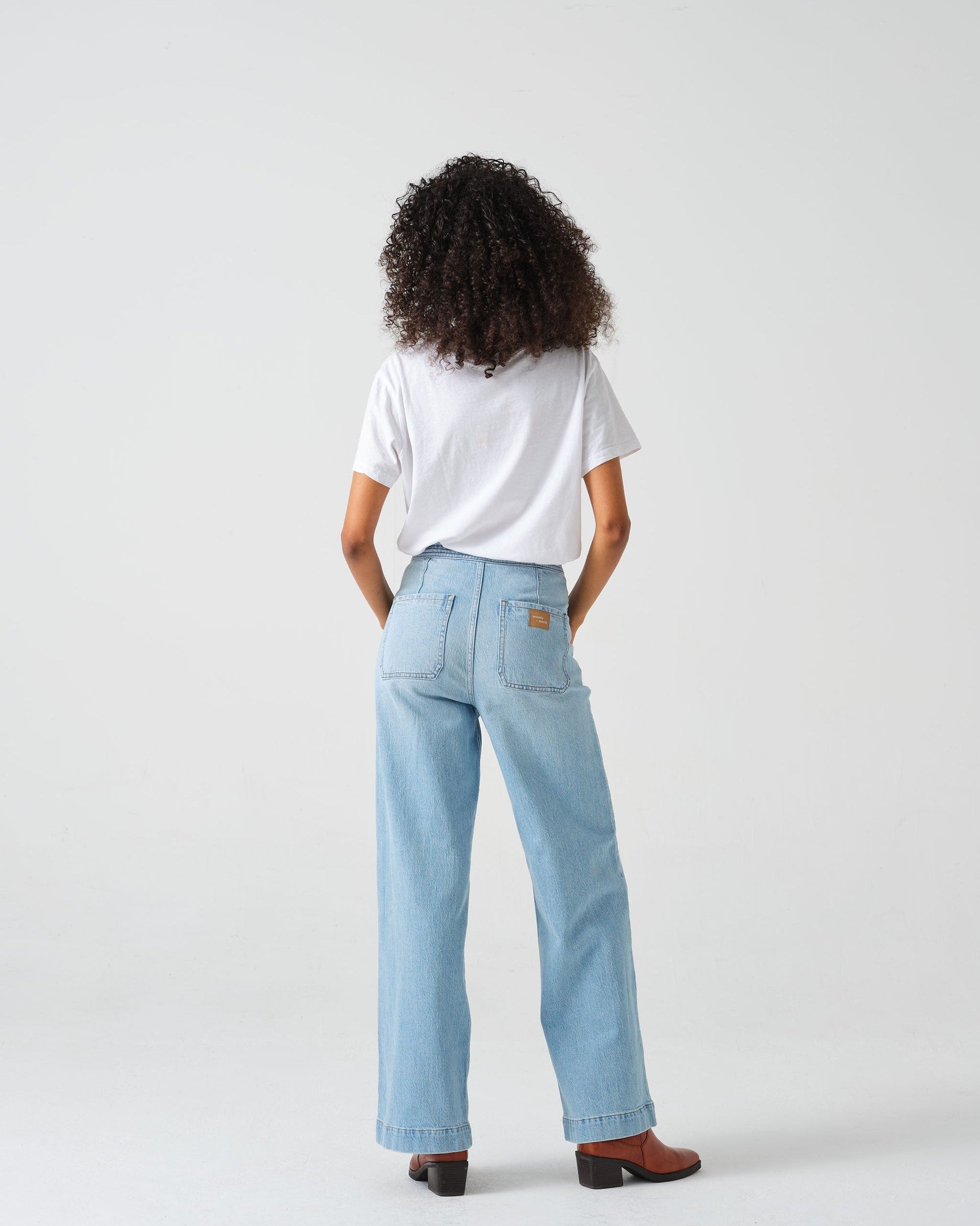 A pair of high-waisted, wide leg jeans with a button-up front in an oceanic blue wash. The jeans are worn with brown ankle boots.