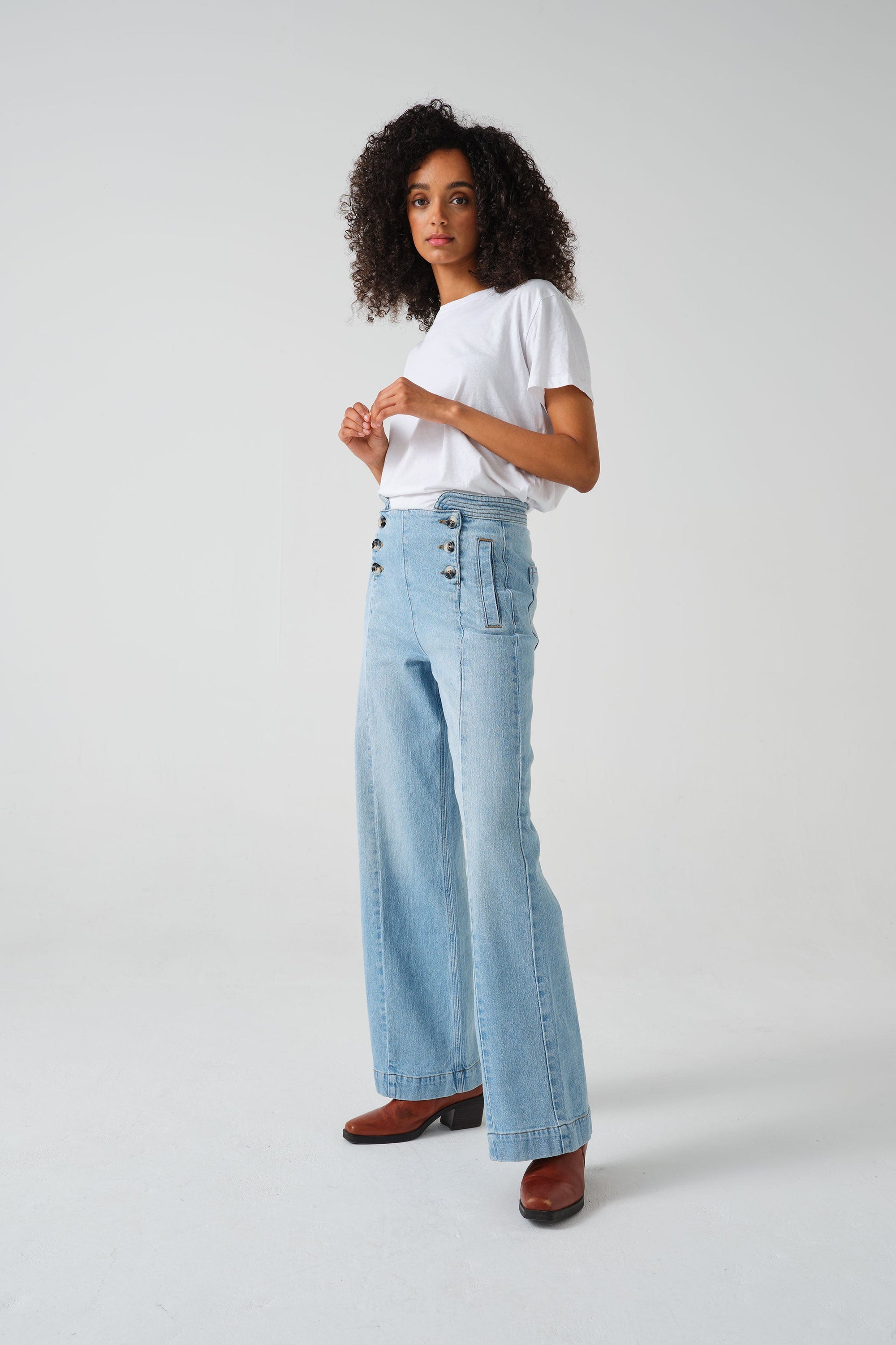 A pair of high-waisted, wide leg jeans with a button-up front in an oceanic blue wash. The jeans are worn with brown ankle boots.