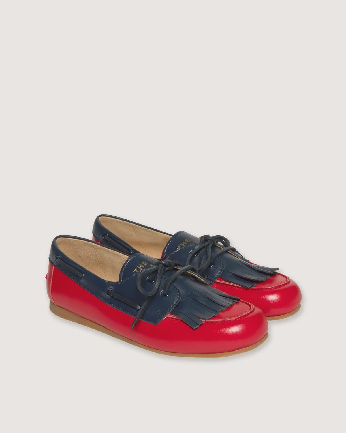 A pair of children's boat-style loafers in navy blue and bright red, shown on a light beige background.