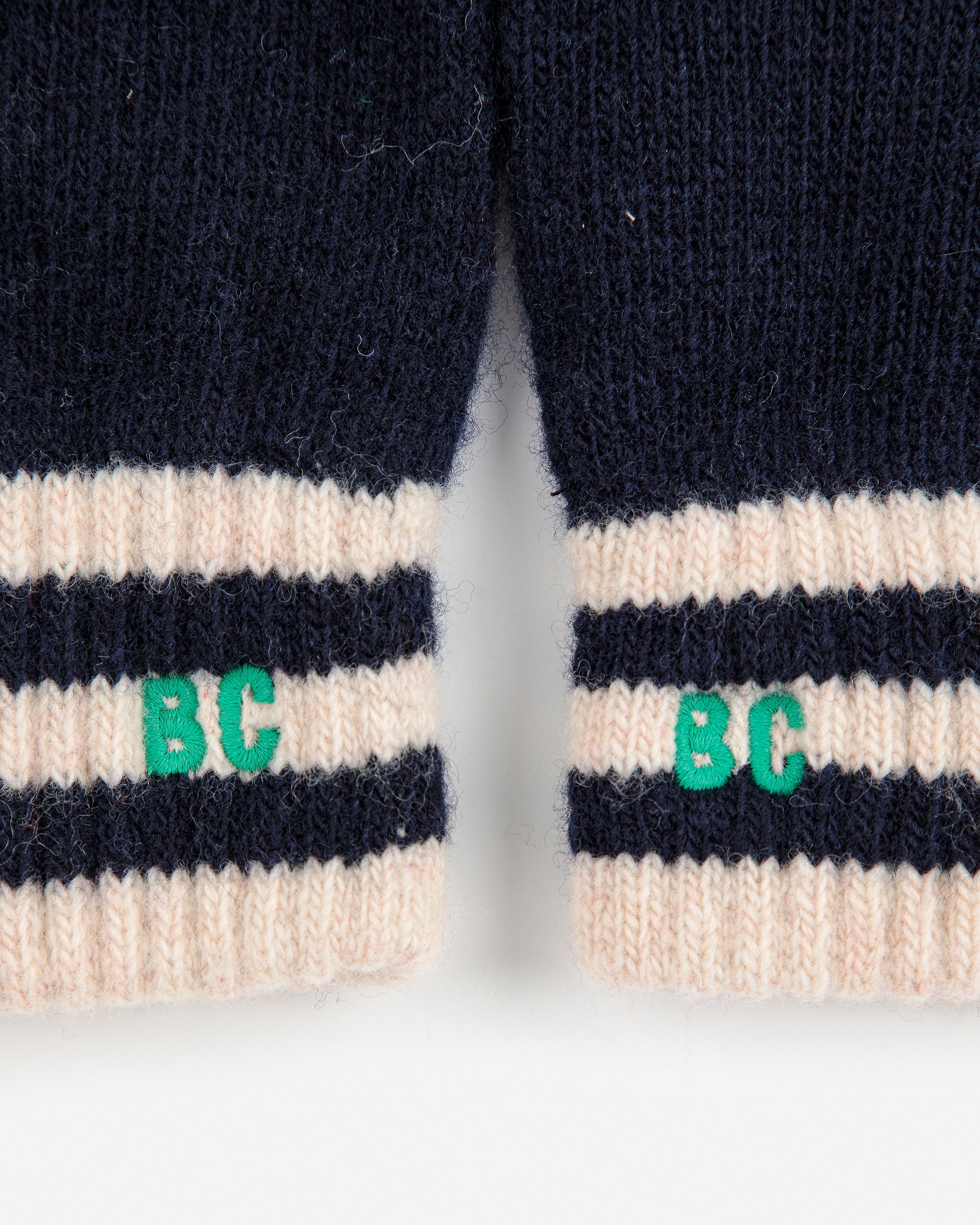 Close-up of navy and beige striped gloves with 'BC' logo on a white background