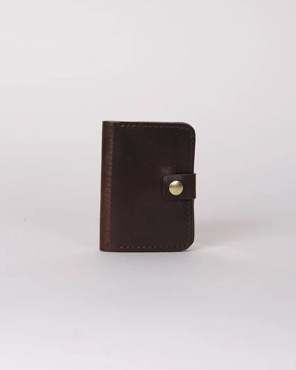 A small dark brown leather card holder or wallet with a snap button closure, standing upright on a light gray background.