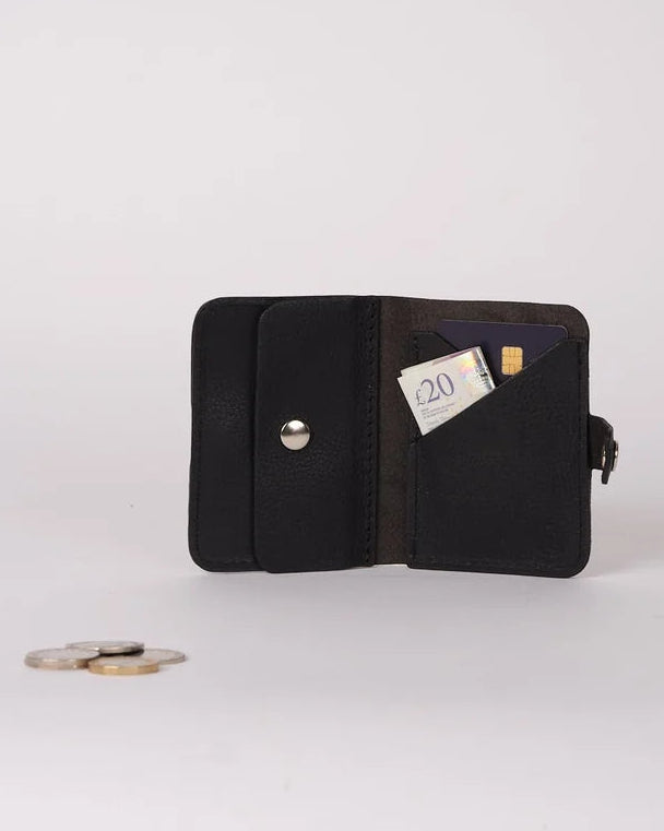 A black leather bifold wallet shown open on a light gray background, with a card partially inserted and a few coins placed in front of it.