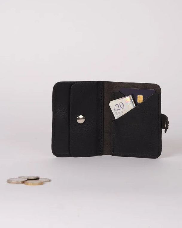 A black leather bifold wallet shown open on a light gray background, with a card partially inserted and a few coins placed in front of it.