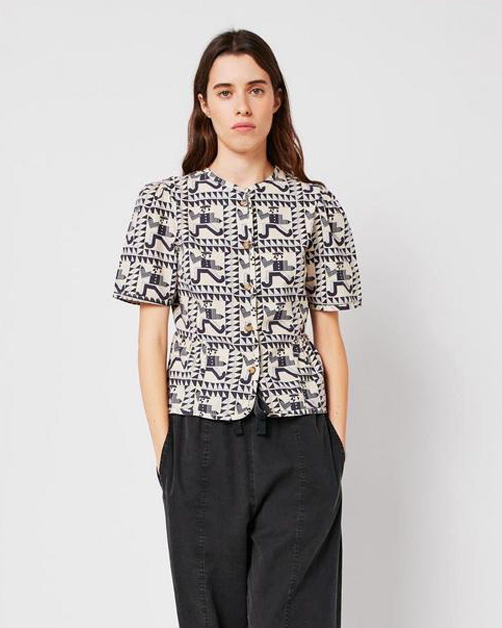 Woman wearing a patterned shirt and dark pants on a plain background