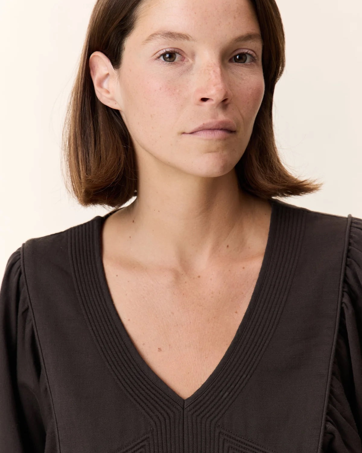 Woman wearing a dark brown top against a plain background