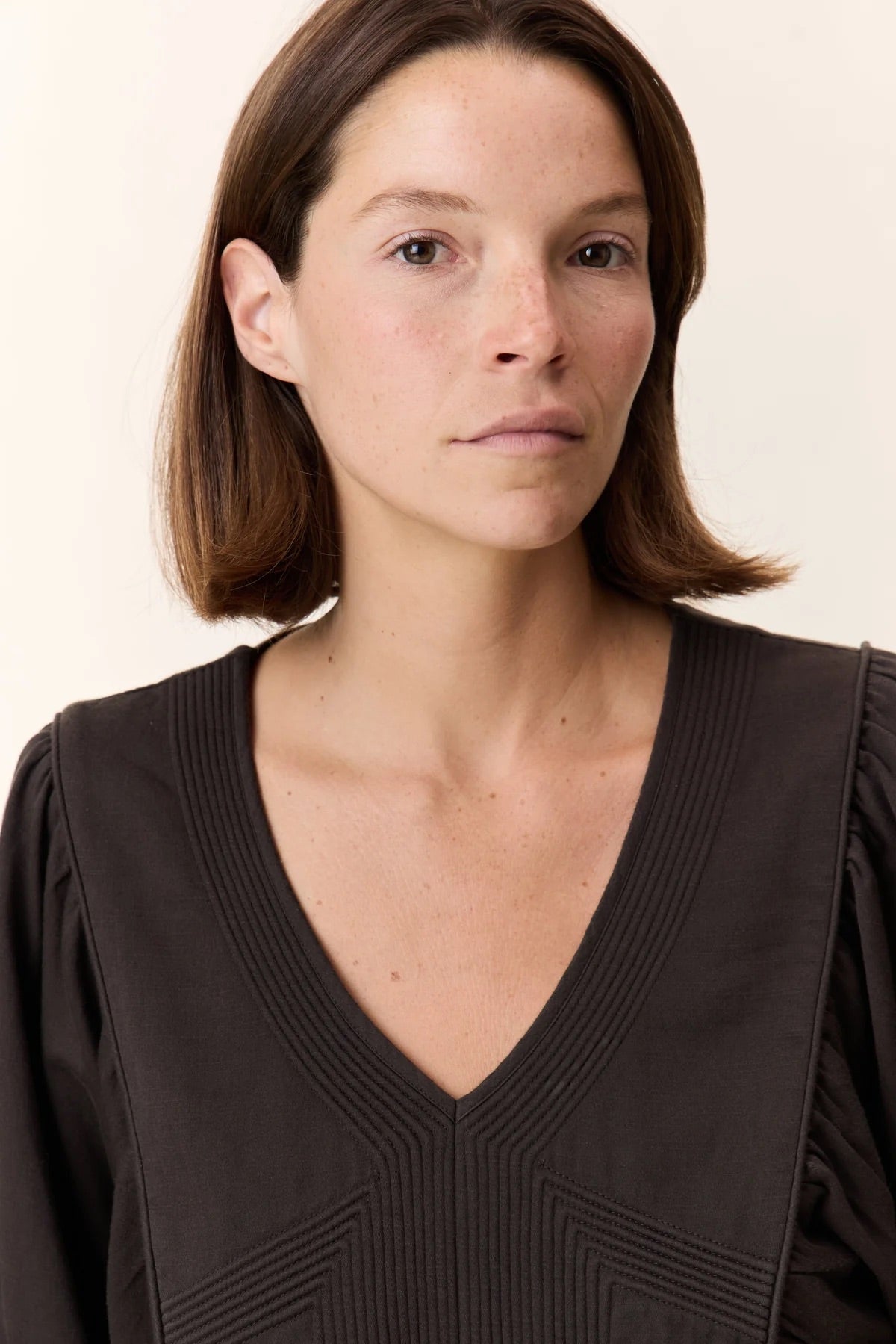 Woman wearing a dark brown top against a plain background