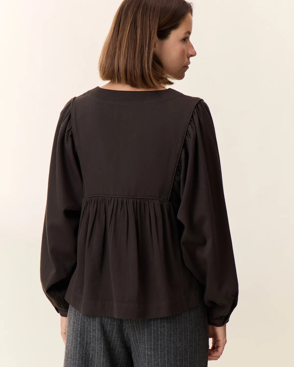 Woman wearing a dark brown blouse with long sleeves on a plain background