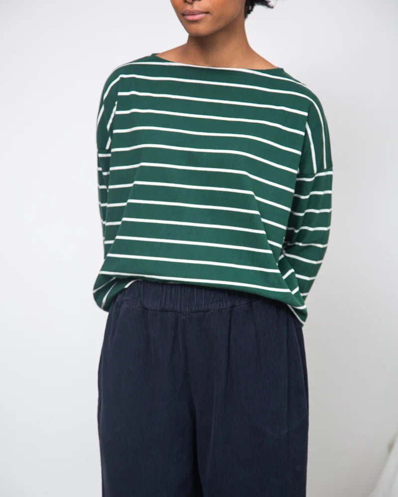 Person wearing a green and white striped sweater with navy pants against a plain background