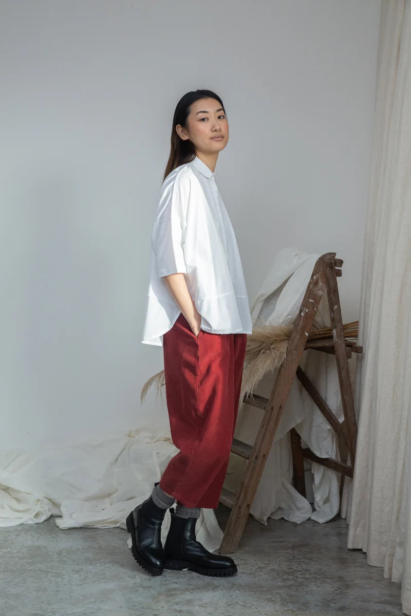 Woman wearing a white shirt and red pants standing in a minimalistic room.