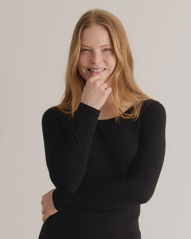 A woman wearing a black long-sleeve top with a crew neck, standing against a neutral background.