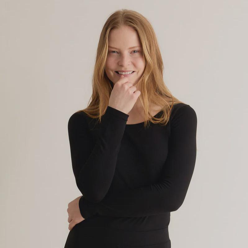 A woman wearing a black long-sleeve top with a crew neck, standing against a neutral background.