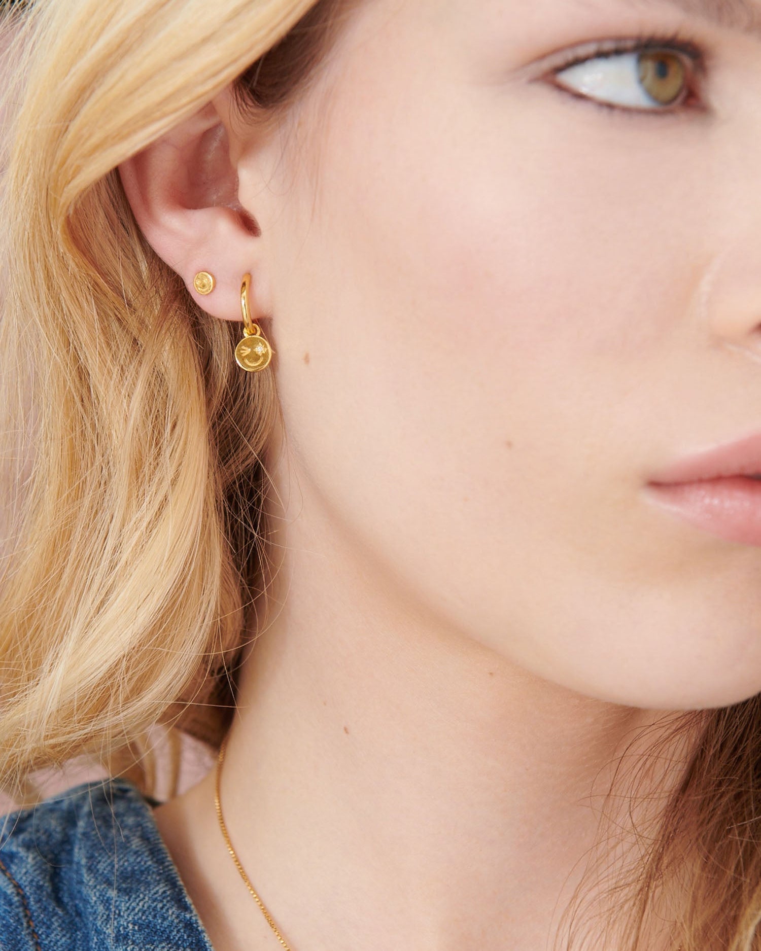 Close-up of a person wearing gold earrings with a neutral background