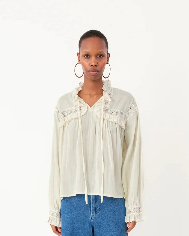Person wearing a white blouse with ruffled details and blue jeans on a white background