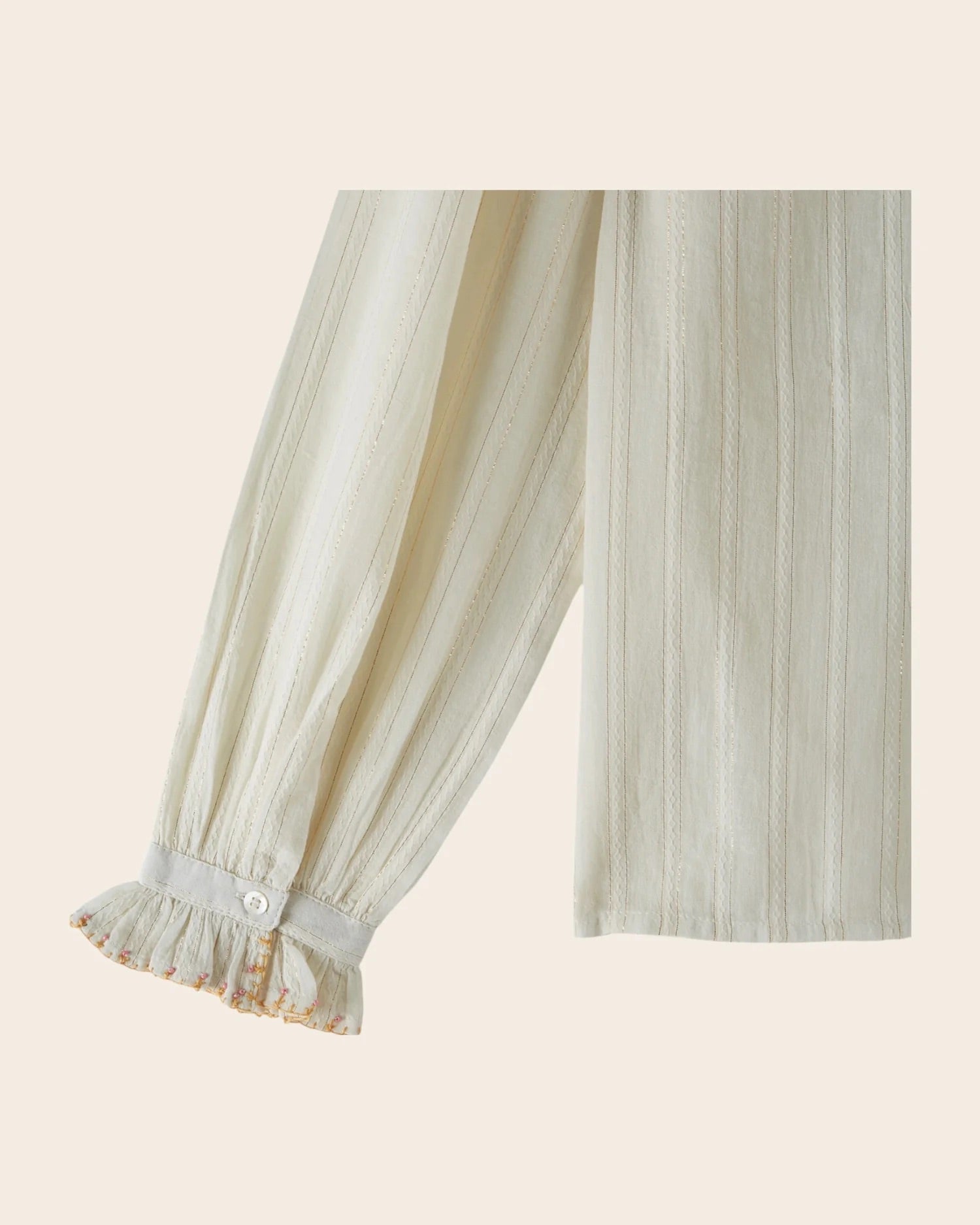 Light-colored pleated blouse with ruffled cuffs on a beige background