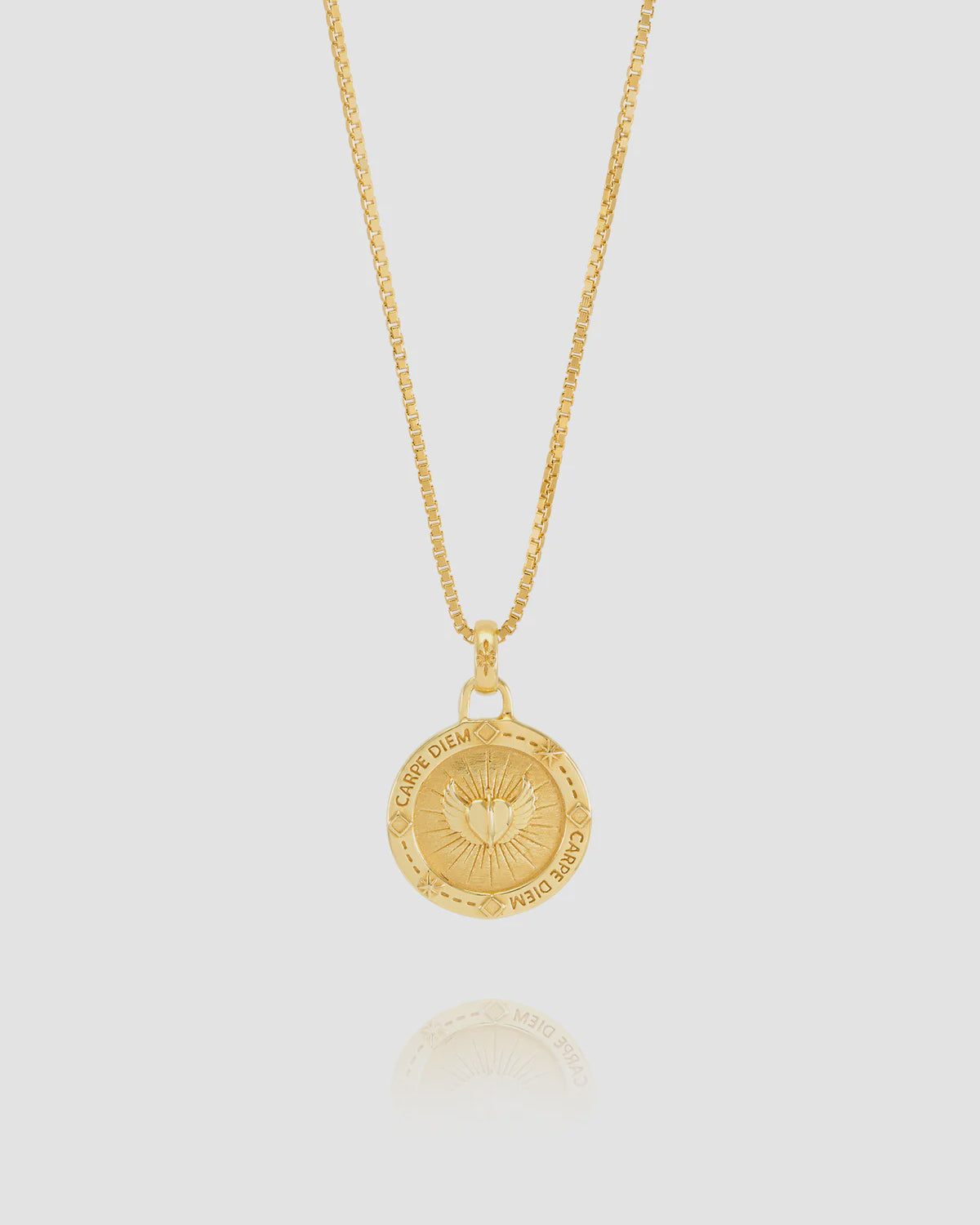 Gold necklace with a circular pendant on a light gray background