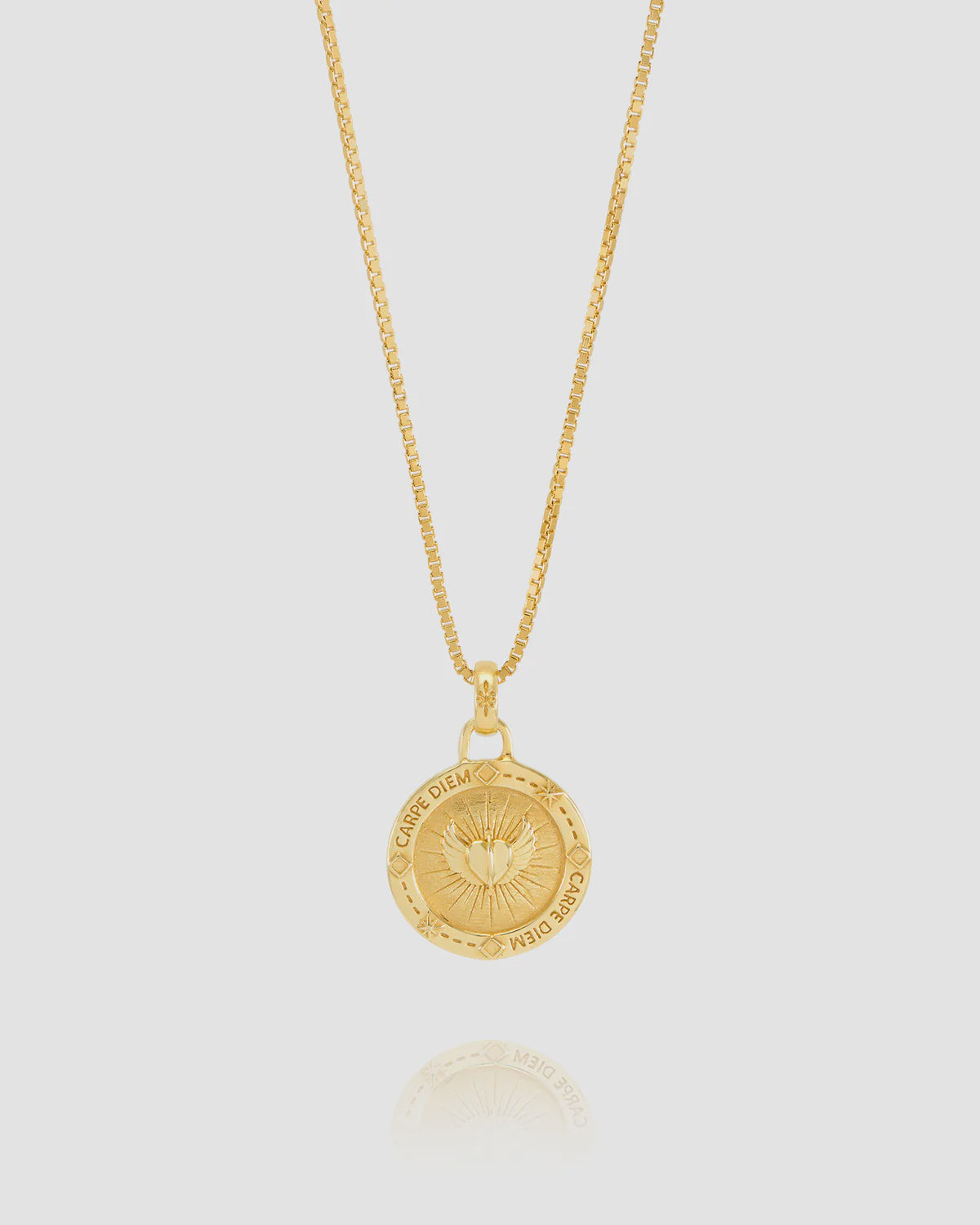 Gold necklace with a circular pendant on a light gray background