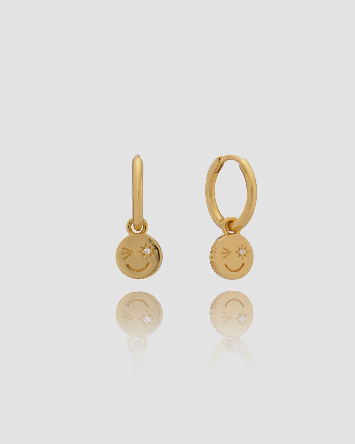 Pair of gold earrings with smiley face charms on a light gray background