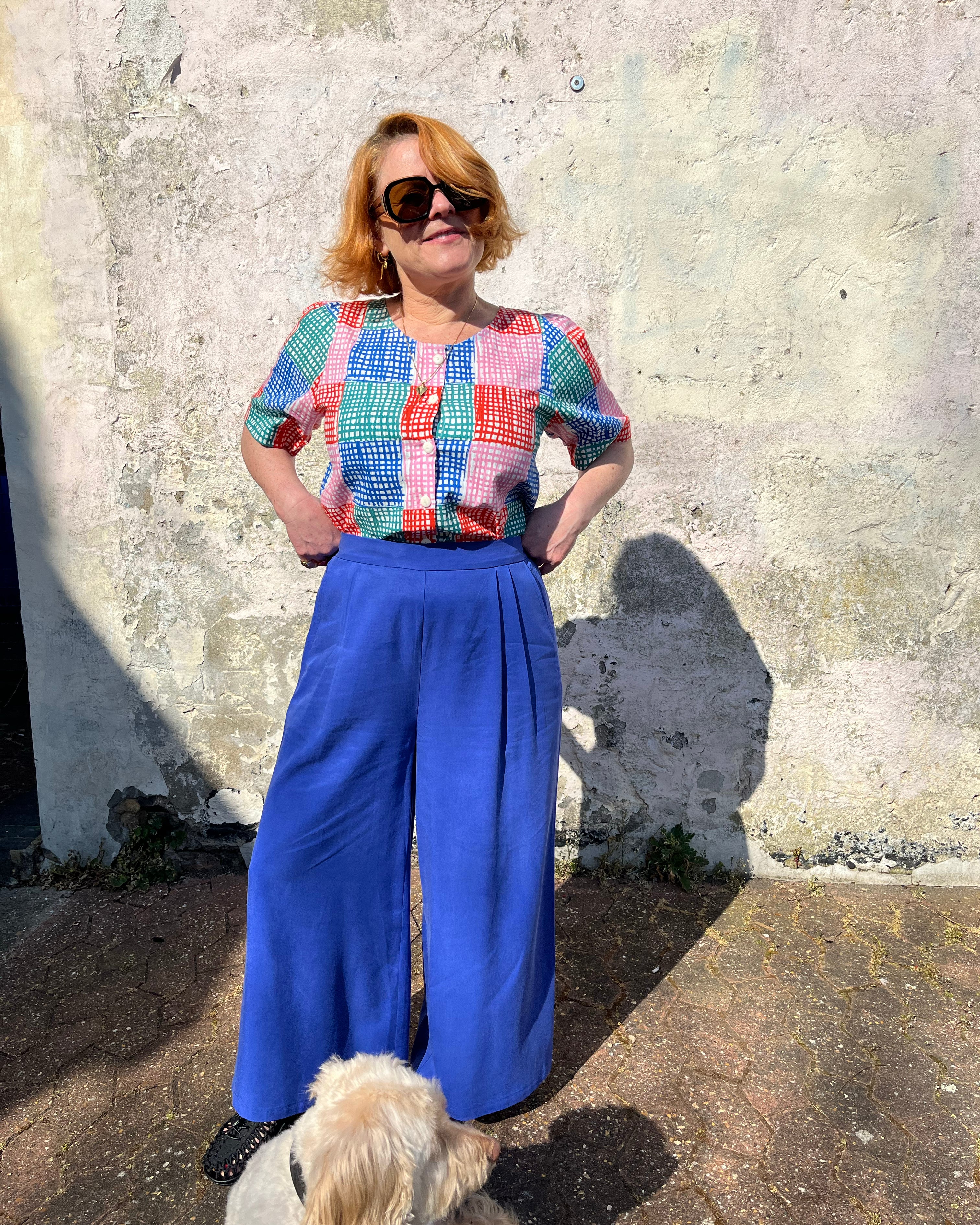 A person standing against a wall wearing cobalt lyocell wide-leg trousers with a flat front waistband, elasticated back, and pleats at the front.