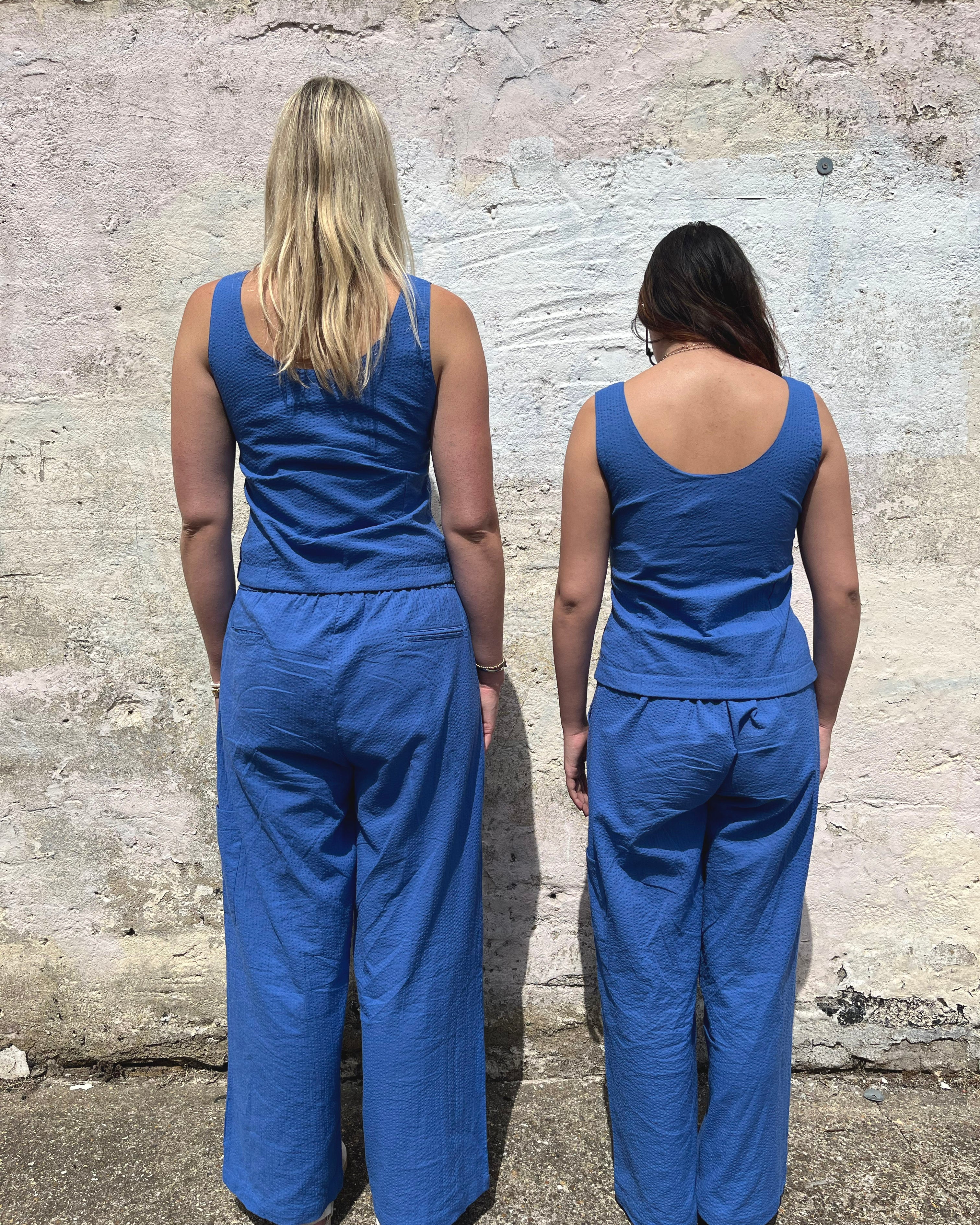 Two people wearing blue jumpsuits standing back-to-back against a textured wall.