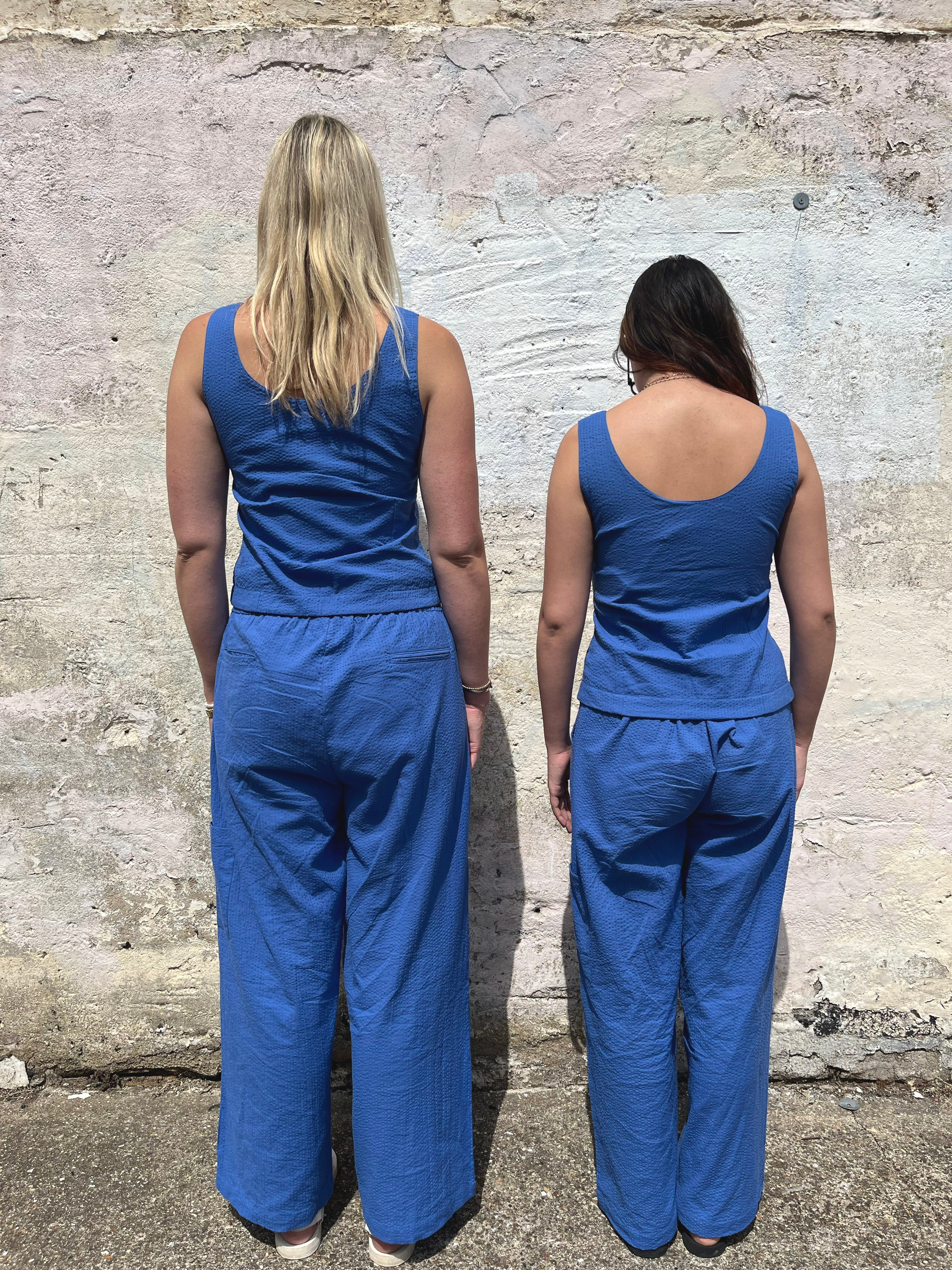 Two people wearing blue jumpsuits standing back-to-back against a textured wall.