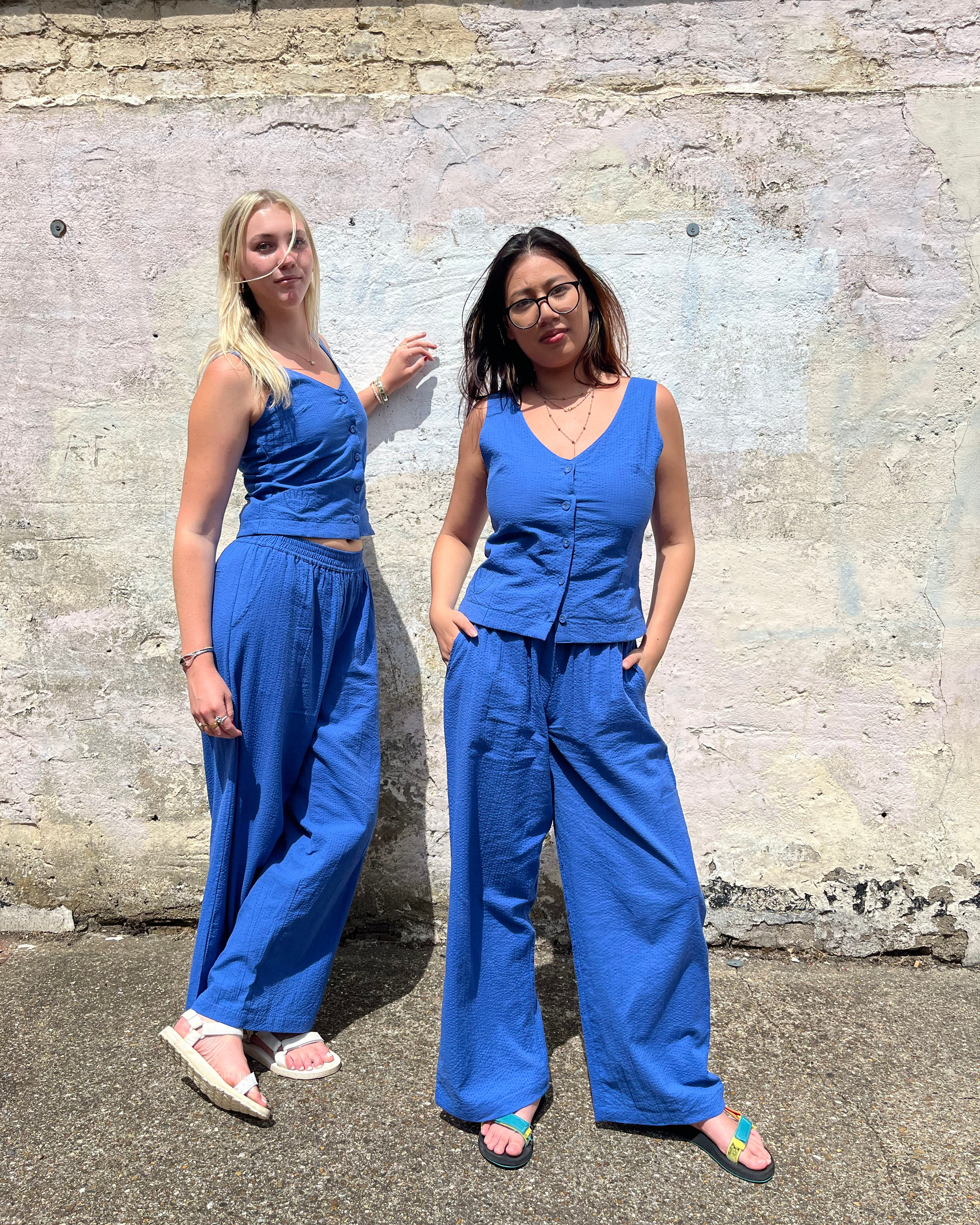 Two women wearing matching blue outfits standing against a textured wall.
