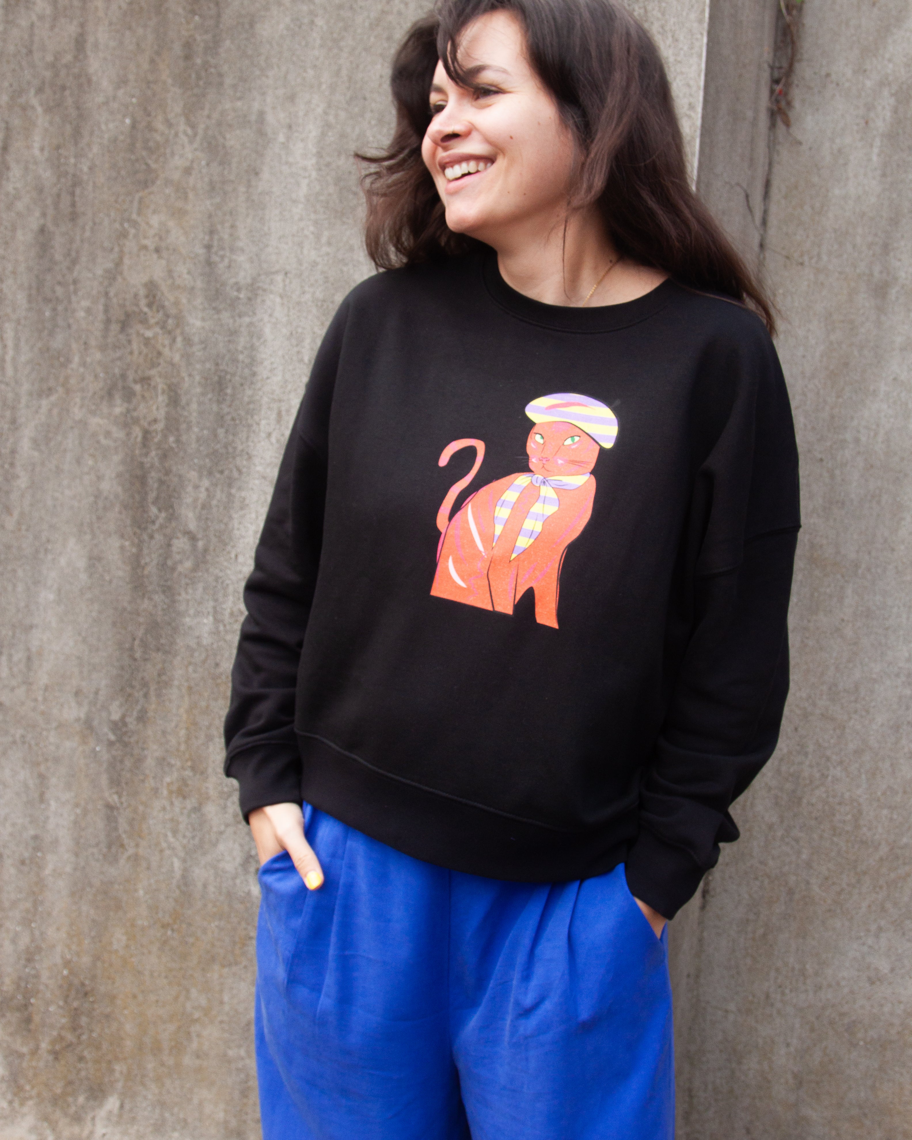 Black sweatshirt with a graphic print of a red and orange cat wearing a Parisian style hat and scarf.