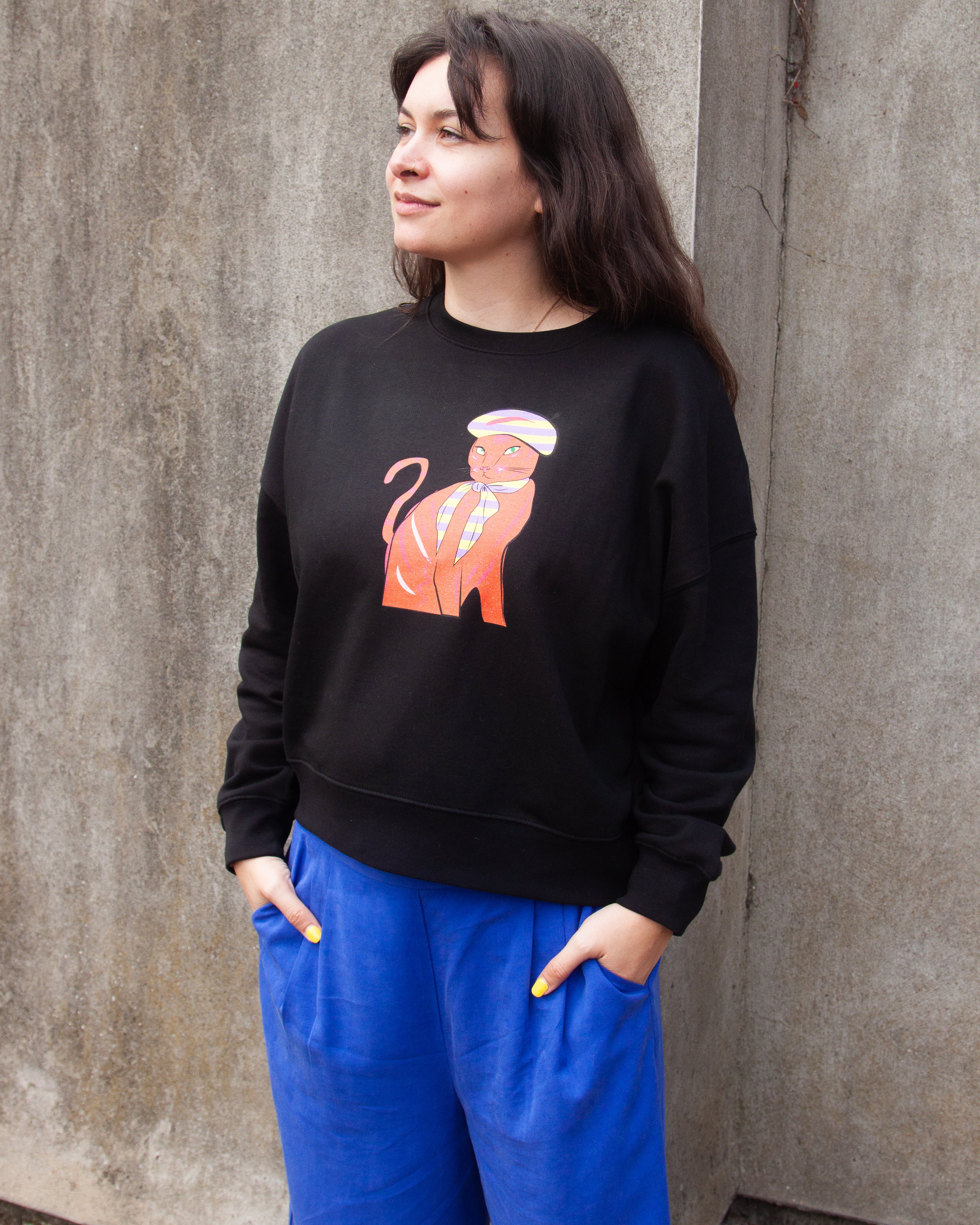 Black sweatshirt with a graphic print of a red and orange cat wearing a Parisian style hat and scarf.