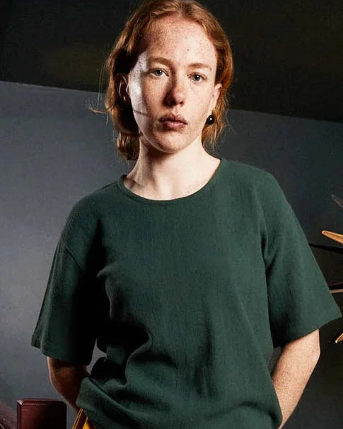 Woman wearing a green top and colorful skirt standing in a room with a decorative light fixture.