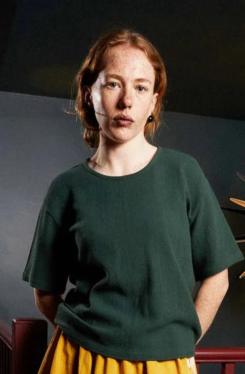 Woman wearing a green top and colorful skirt standing in a room with a decorative light fixture.