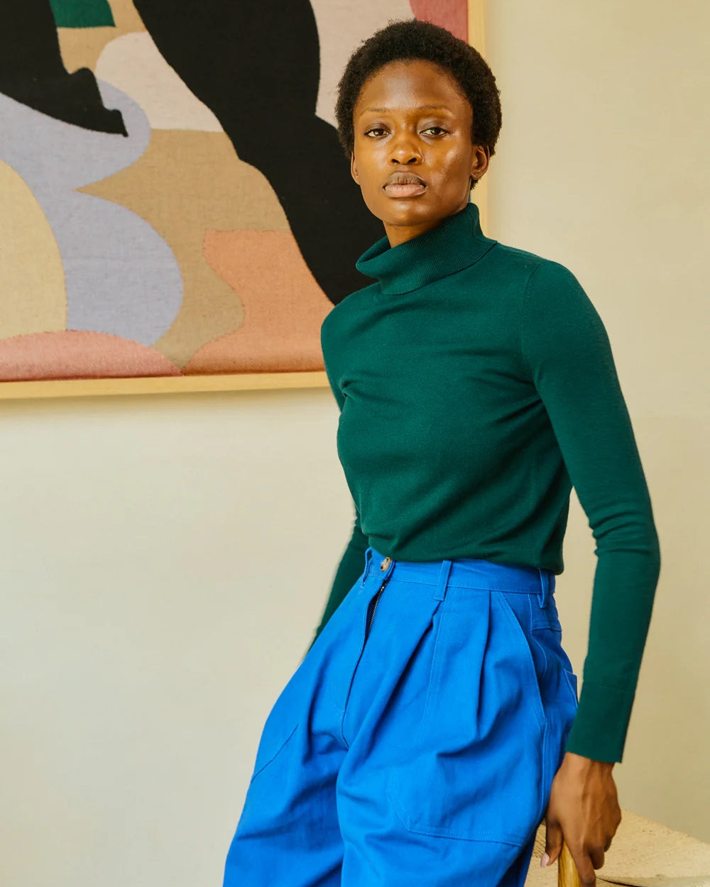 Person wearing a green top and blue pants in a room with abstract art on the wall.