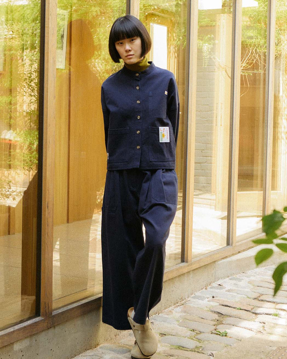 Person wearing a navy blue outfit standing in front of a glass building.