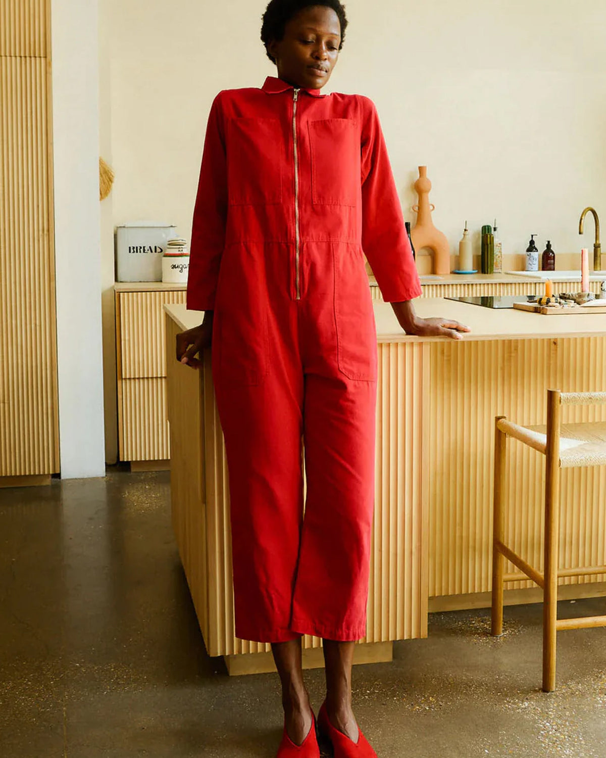 Person wearing a red jumpsuit standing in a kitchen.