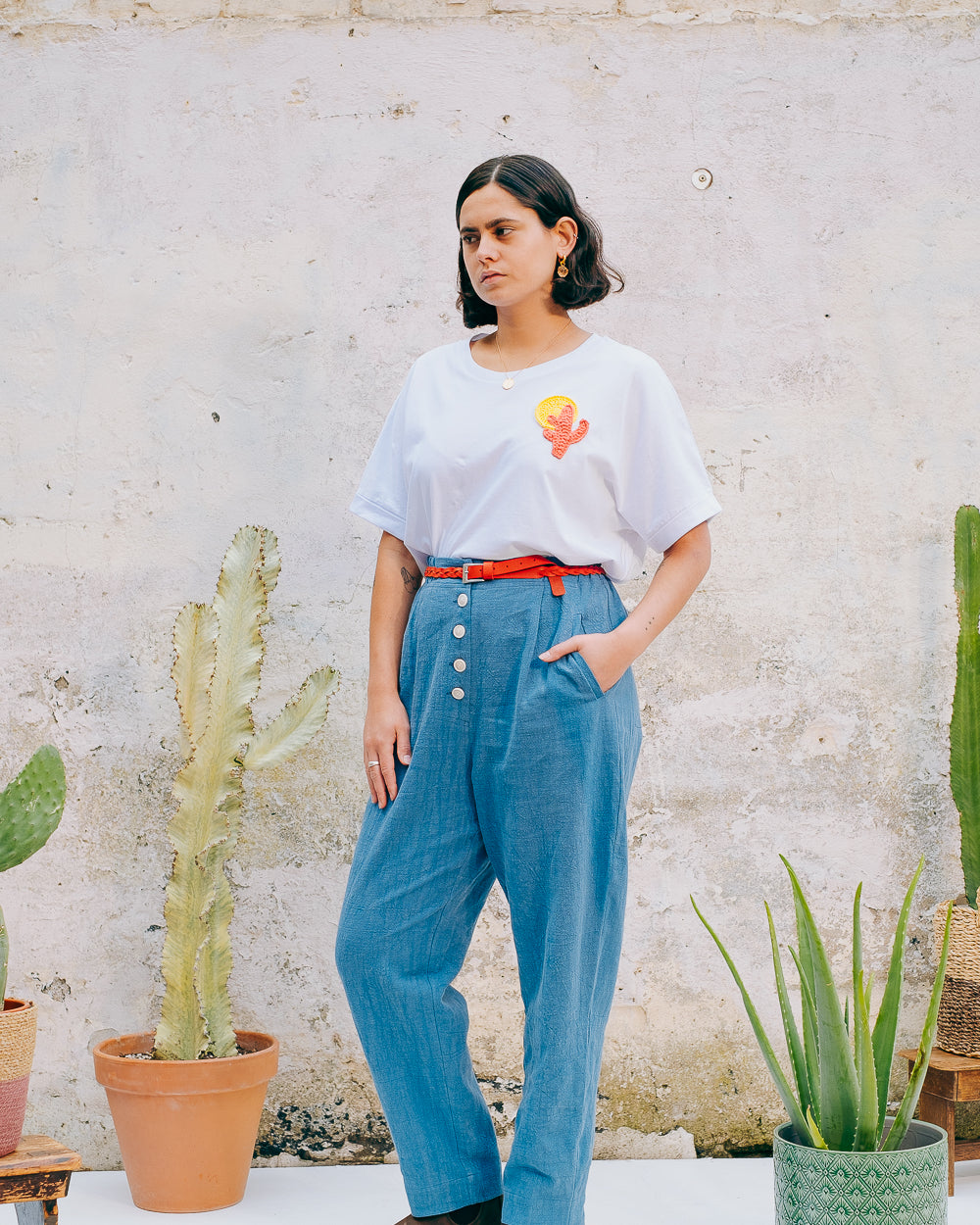A person wearing a white crew neck t-shirt with a hand-crocheted red and yellow cactus and sun motif, paired with a blue skirt and a red belt.