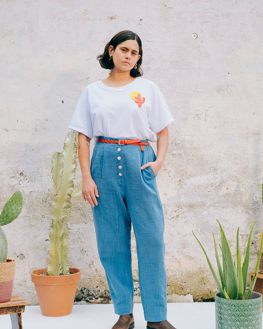 A person wearing a white crew neck t-shirt with a hand-crocheted red and yellow cactus and sun motif, paired with a blue skirt and a red belt.