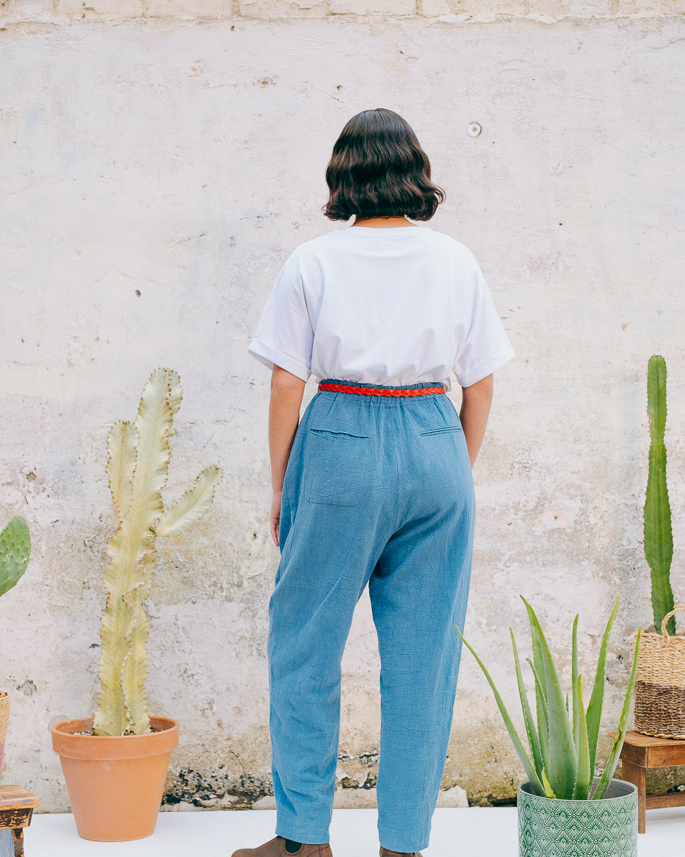 A person wearing a white crew neck t-shirt with a hand-crocheted red and yellow cactus and sun motif, paired with a blue skirt and a red belt.